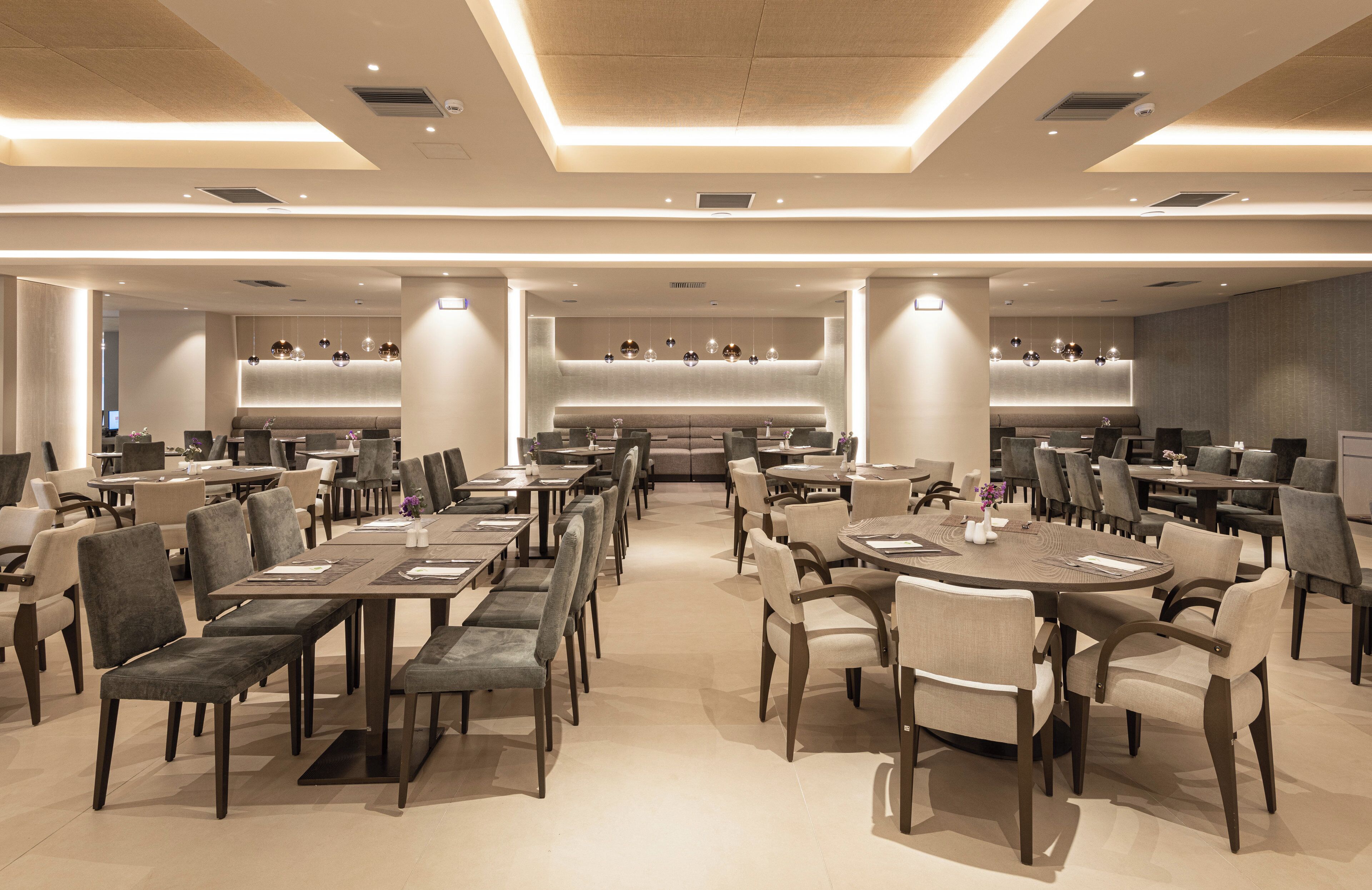 Ein geräumiges Restaurant mit mehreren Essbereichen, darunter runde Tische und gemütliche Sitzgruppen, sowie einer zentralen Bar.