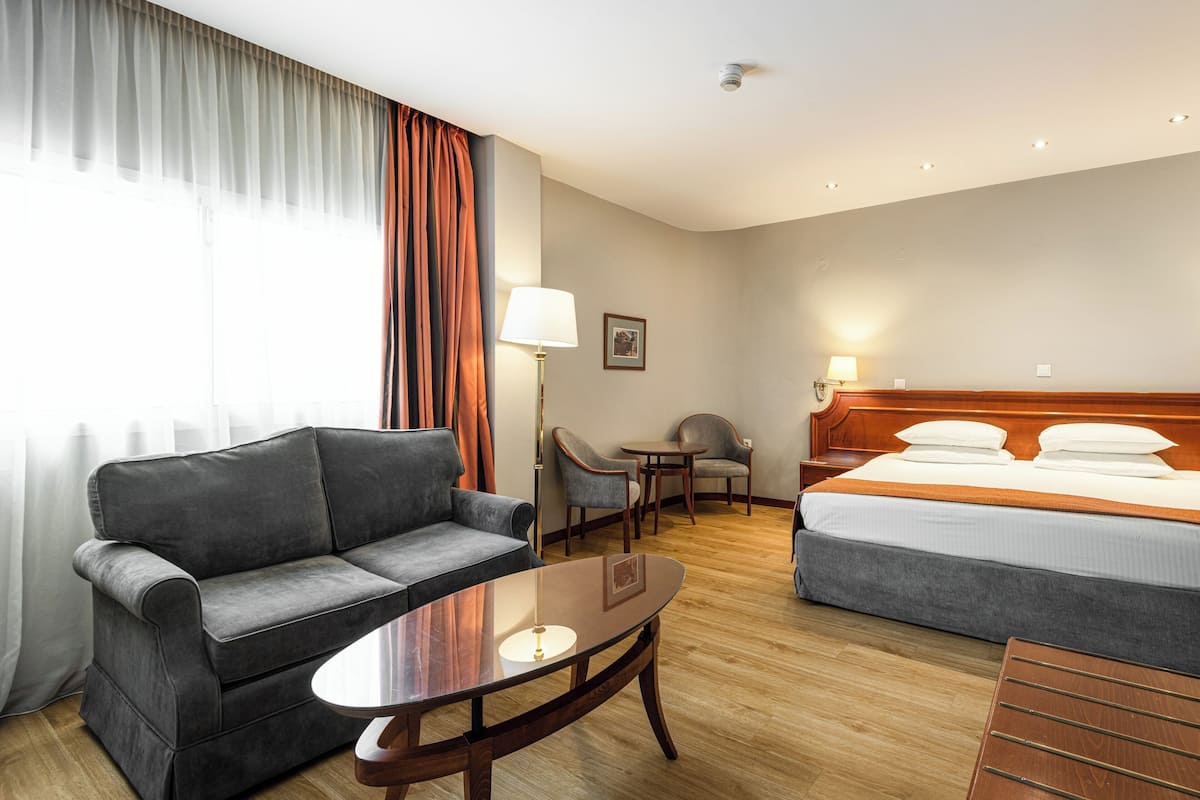 A hotel room with a bed, a sofa, a small table, a chair, and a lamp.