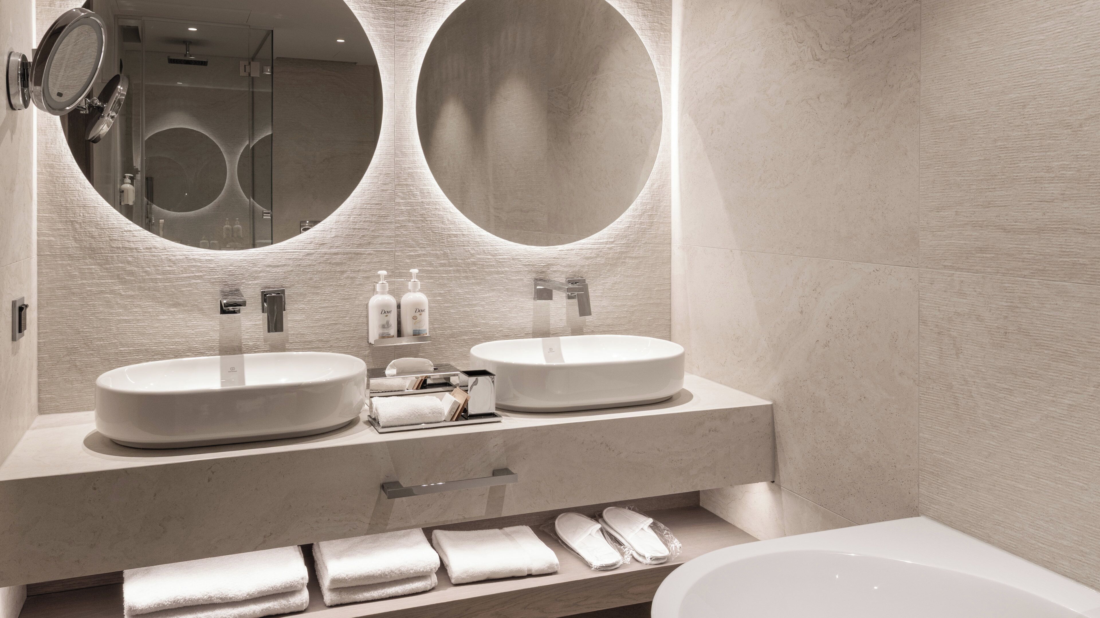 A modern bathroom with two sinks, a large mirror, and a bathtub.