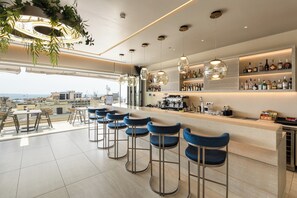 Zona de bar moderna con una barra larga, varios taburetes y vistas a la ciudad.
