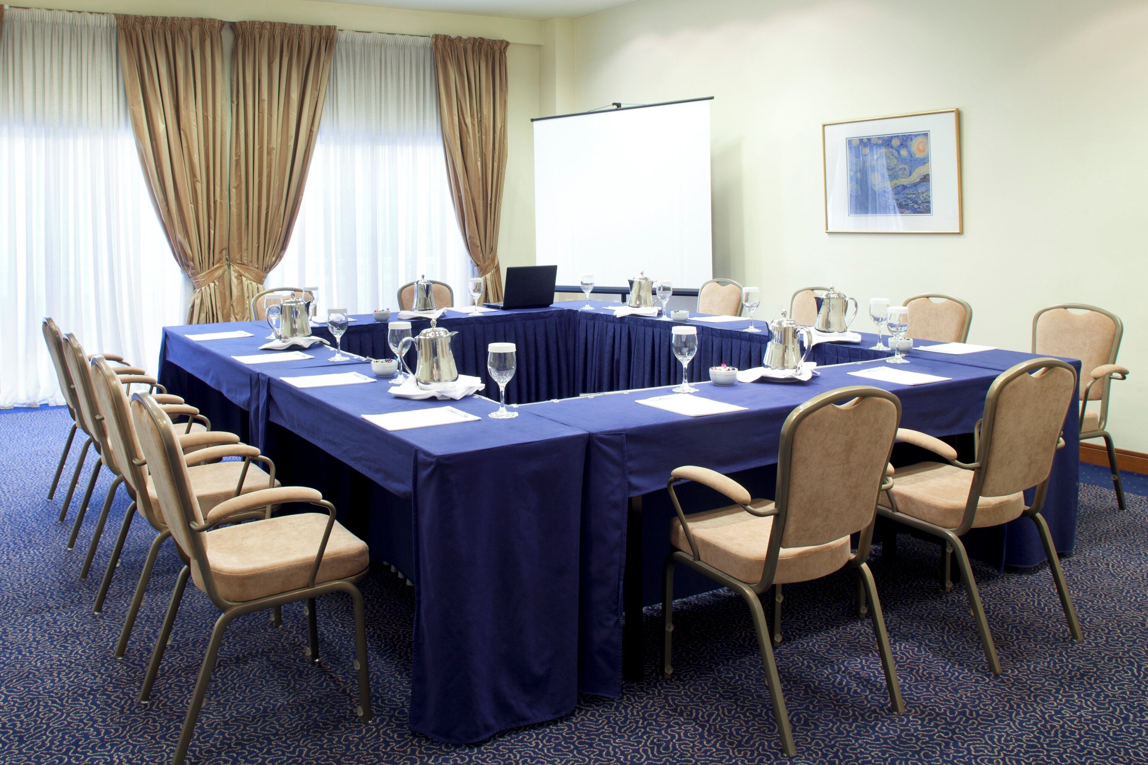 Un salón de conferencias con una larga mesa, sillas y una pantalla para proyector.