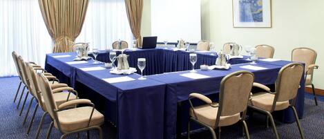 Un salón de conferencias con una larga mesa, sillas y una pantalla para proyector.