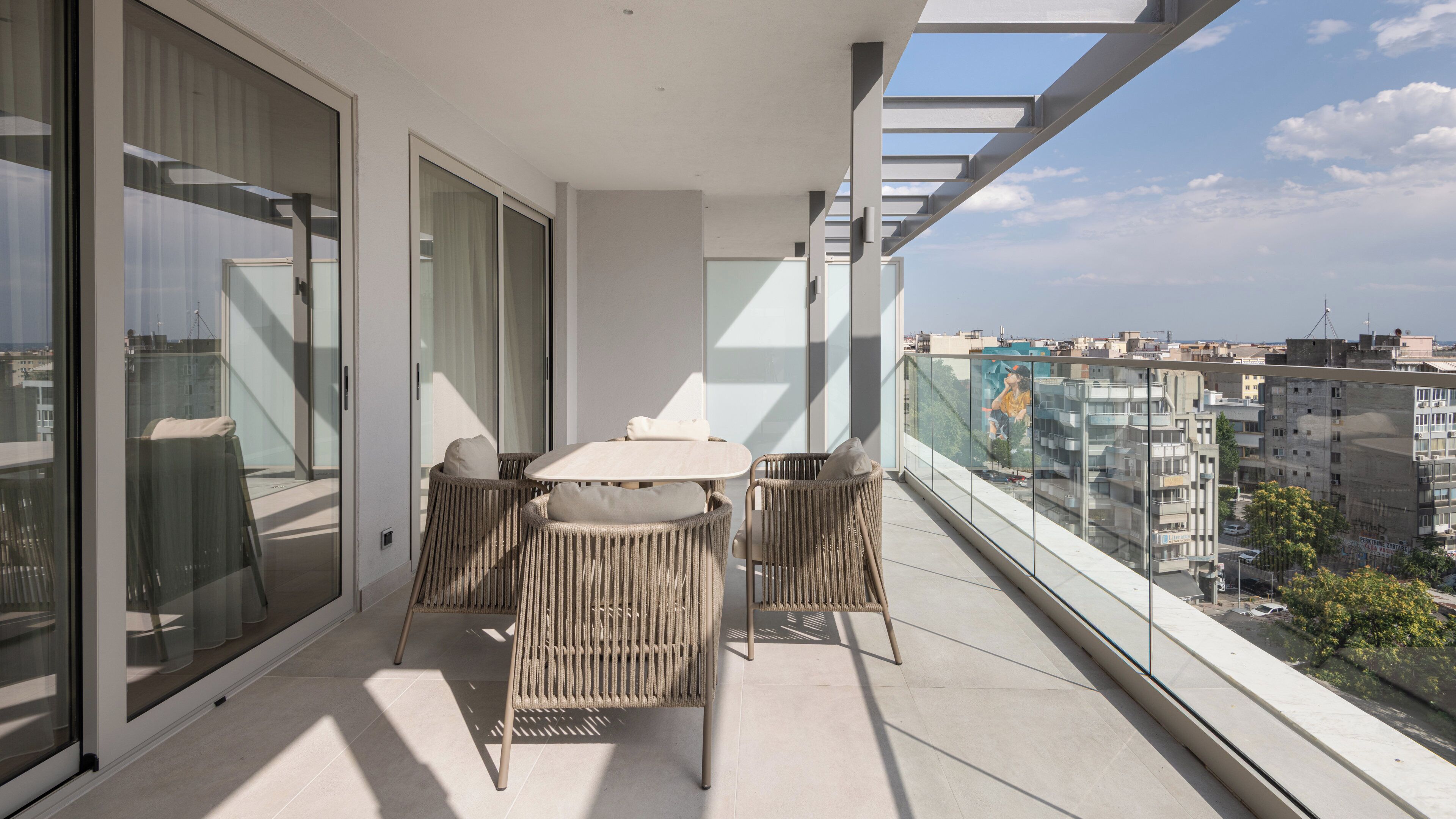 A balcony with a table and chairs, large windows, and a view of the cityscape.