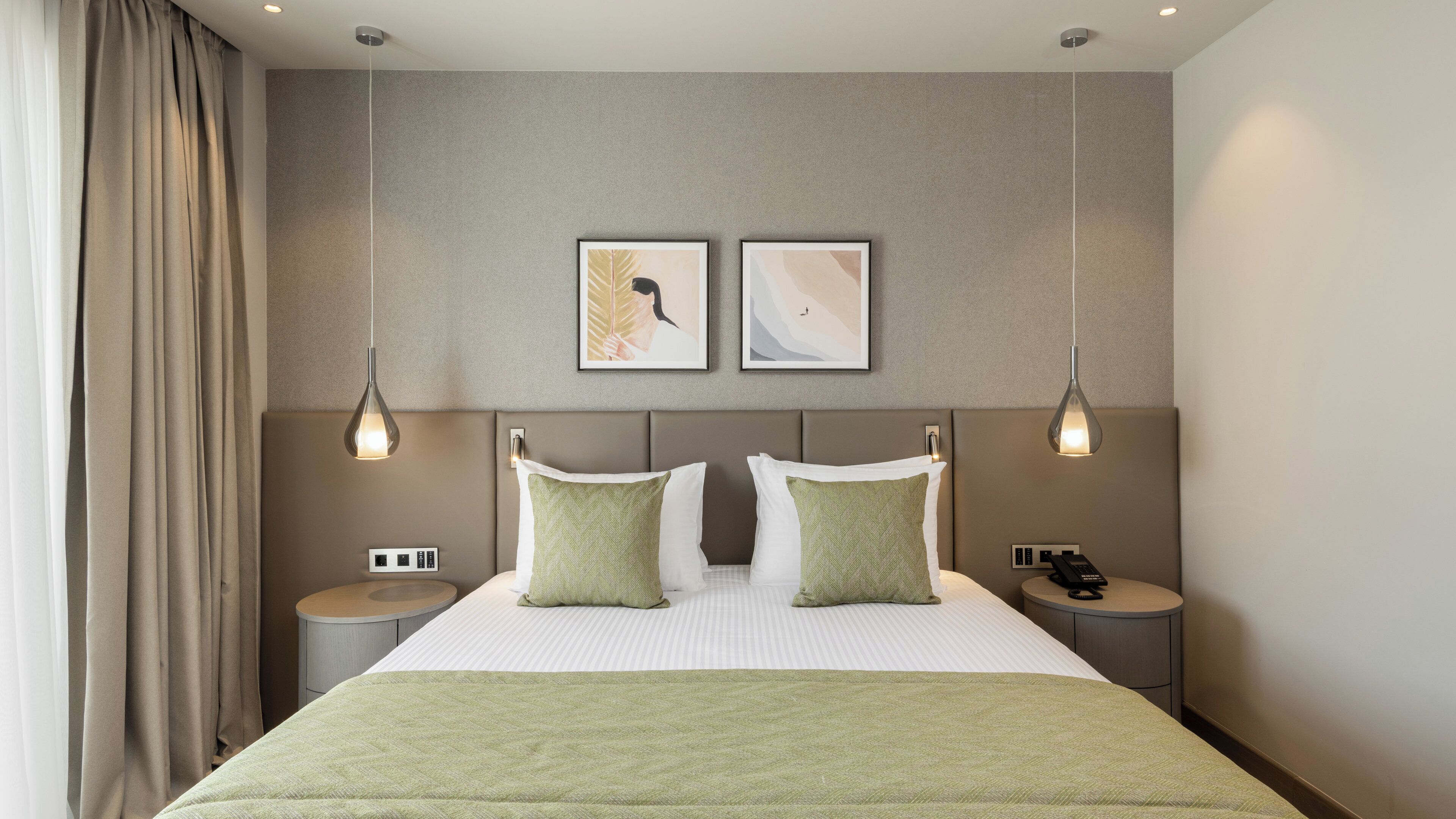 A hotel room with a bed, two bedside tables, a wall-mounted telephone, and two pendant lights.