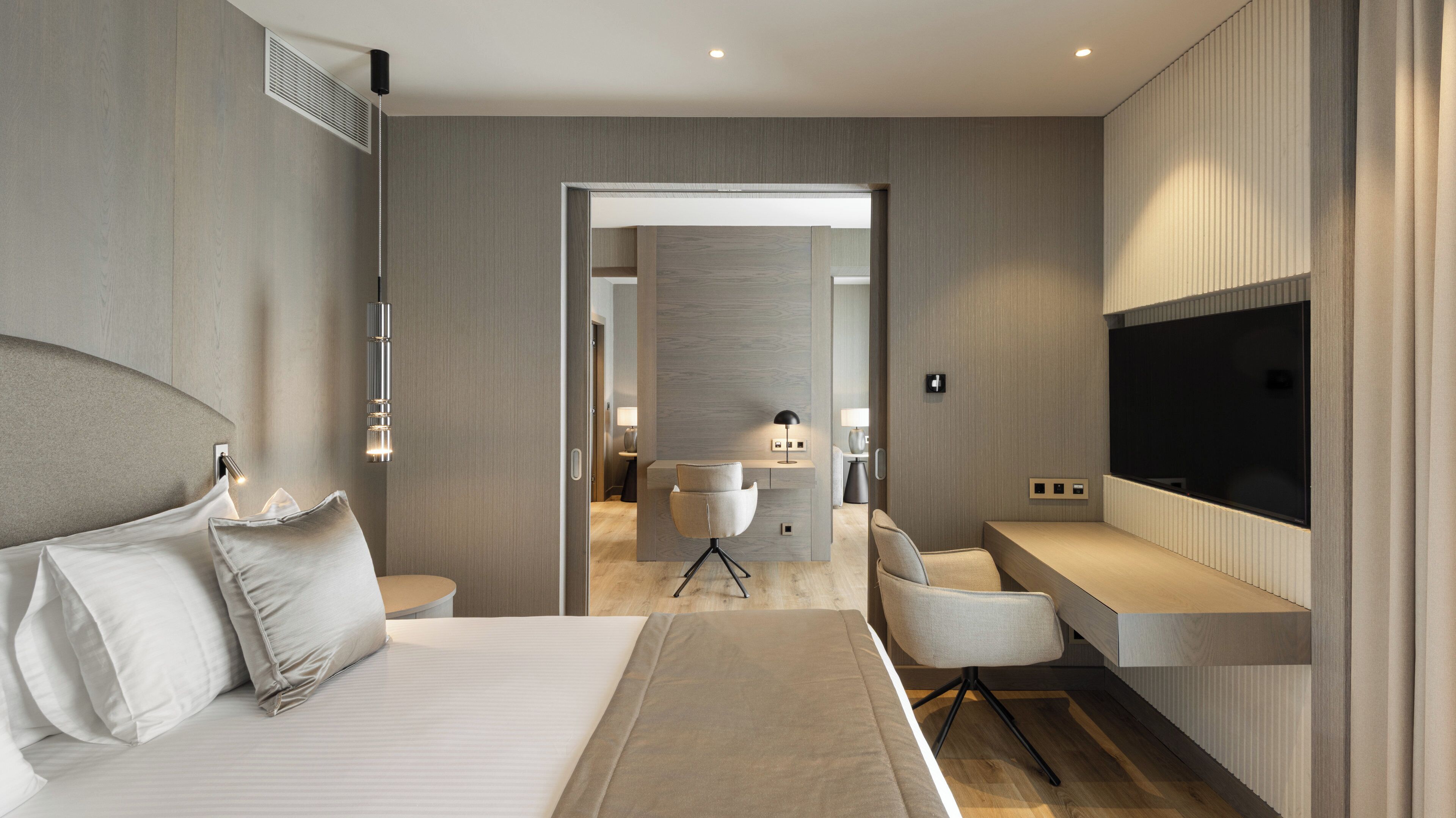 Una habitación de hotel moderna con una cama grande, un escritorio, una silla, un televisor y un baño visible a través de una puerta abierta.