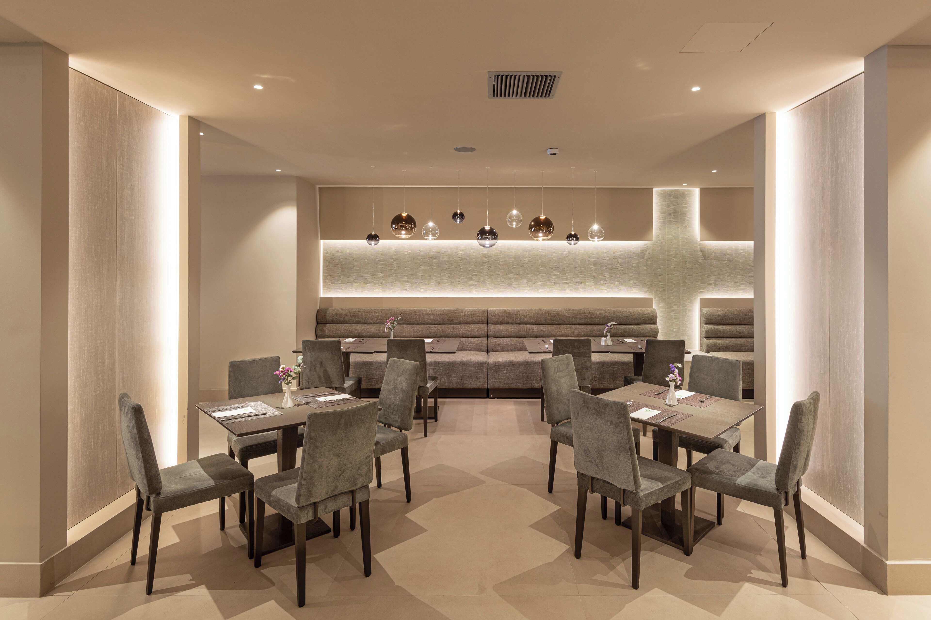 A modern dining area with a long table and multiple chairs, a seating area with sofas, and a decorative light fixture above the seating.