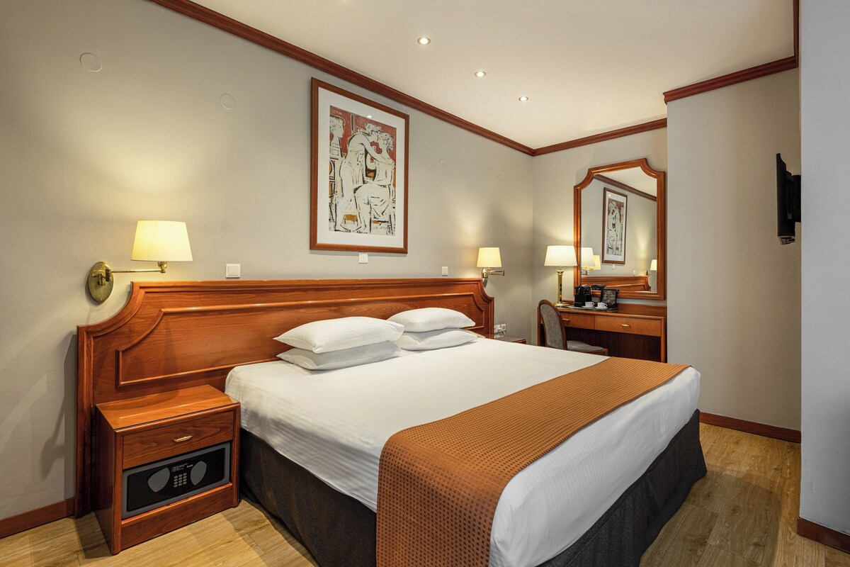 A hotel room with a large bed, bedside tables, a desk, and a mirror.