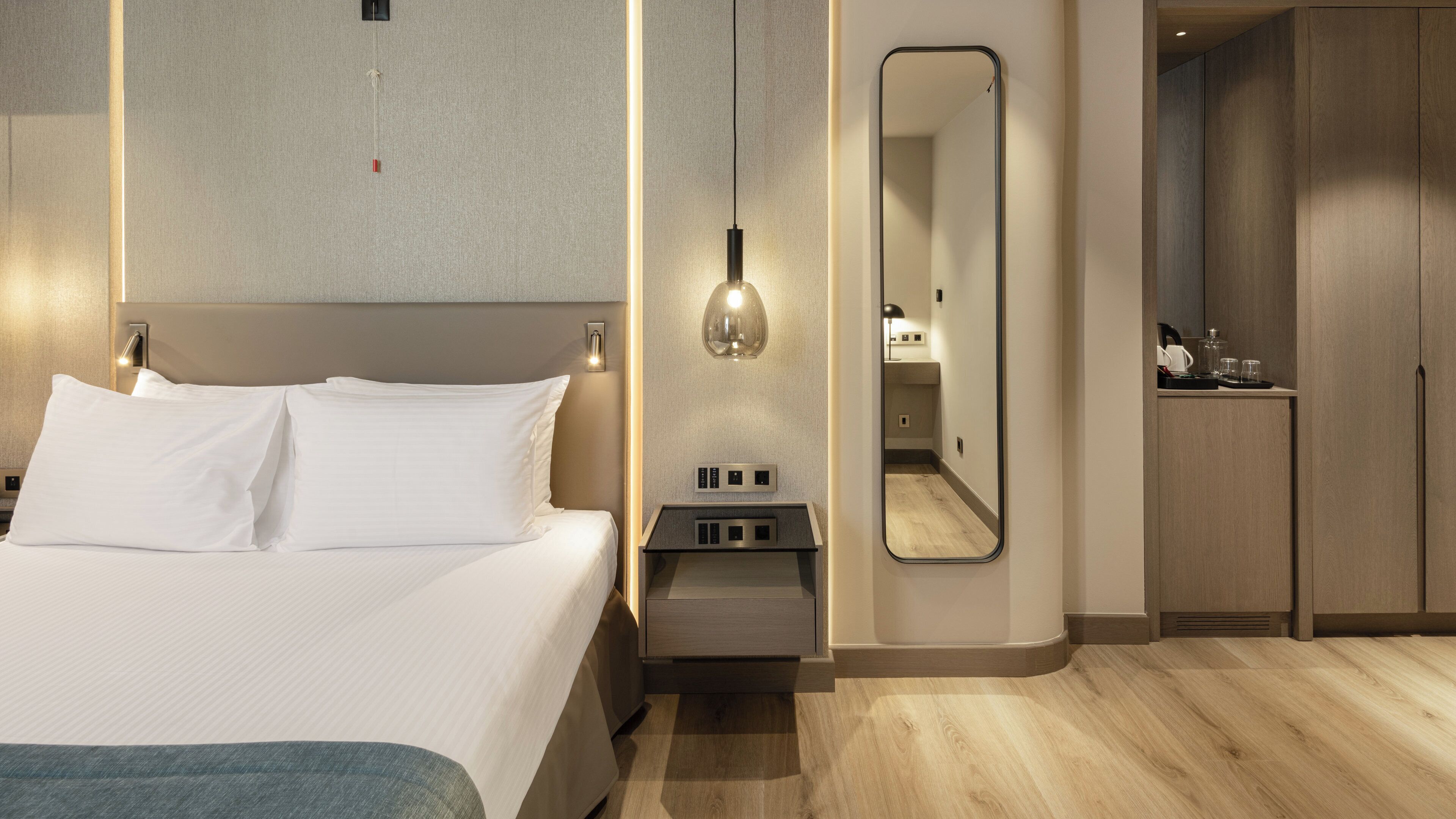 Une chambre d’hôtel moderne équipée d’un lit, d’une table de chevet, d’une lampe, d’un miroir et d’une armoire.