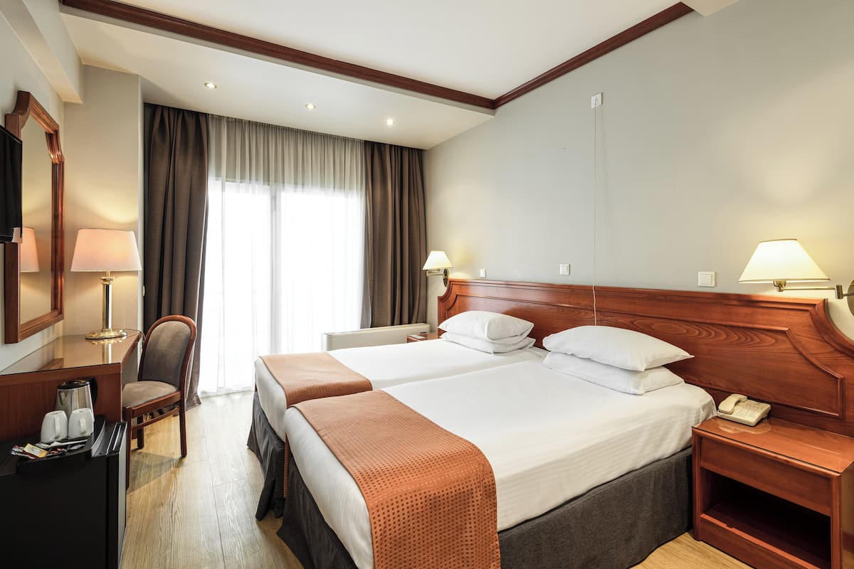 A hotel room with two beds, a desk with a coffee maker, a chair, a telephone, and a window with curtains.
