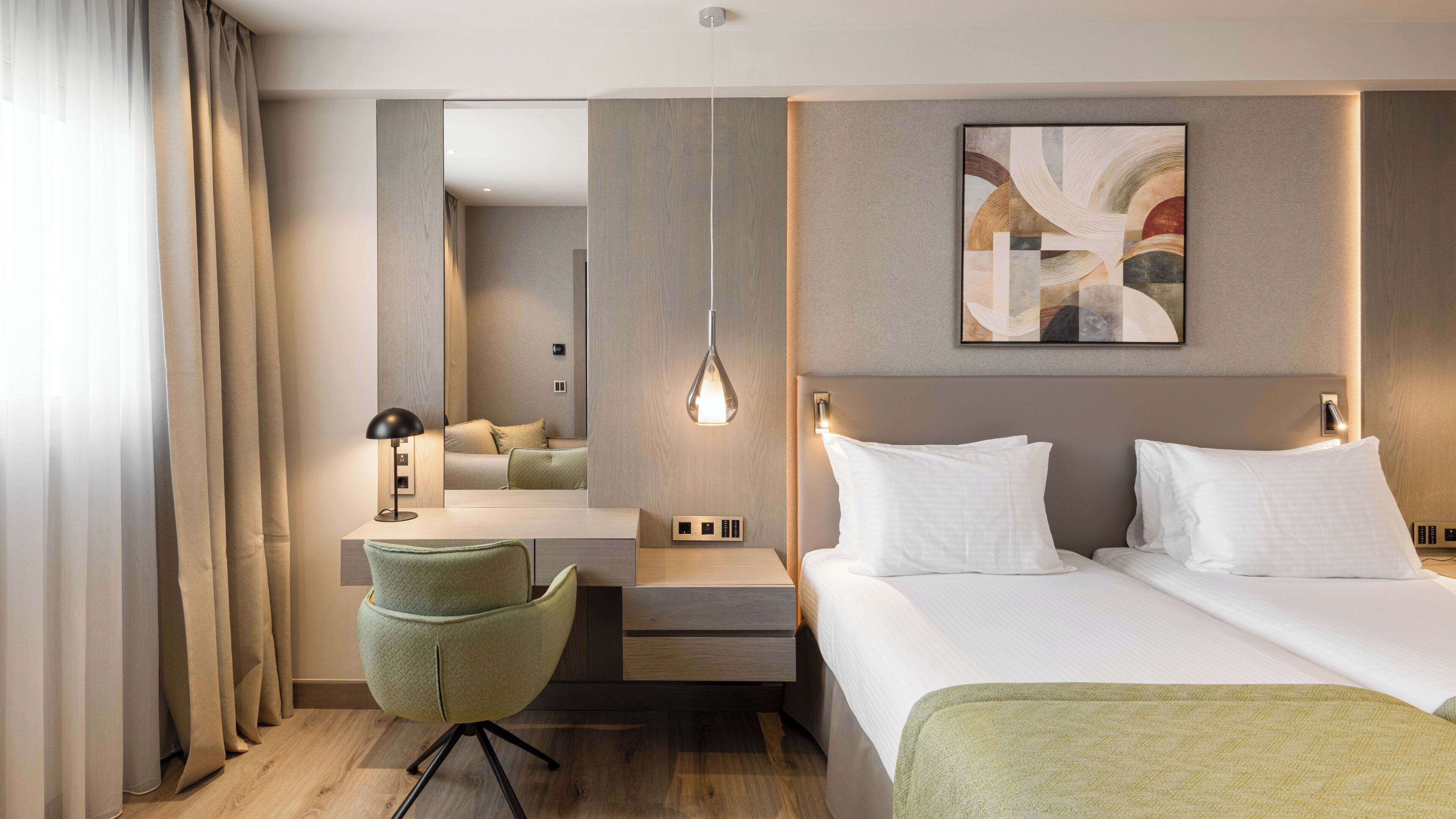 A hotel room with a bed, a desk, a chair, a bedside table, a lamp, and a painting on the wall.
