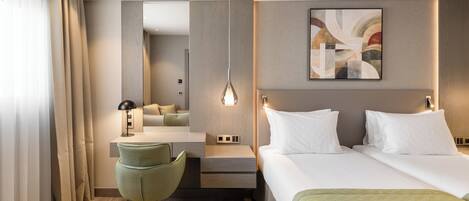 A hotel room with a bed, a desk, a chair, a bedside table, a lamp, and a painting on the wall.