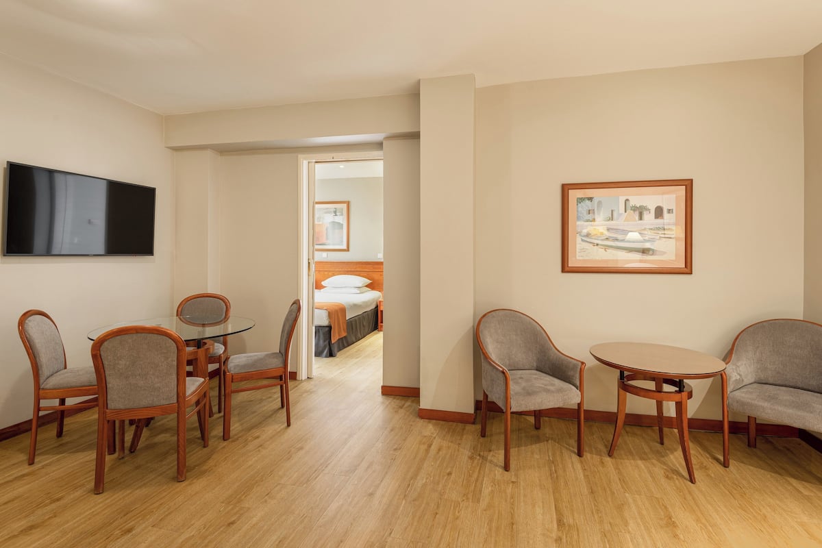 A hotel room with a dining area, a bed, a TV, and a framed picture on the wall.