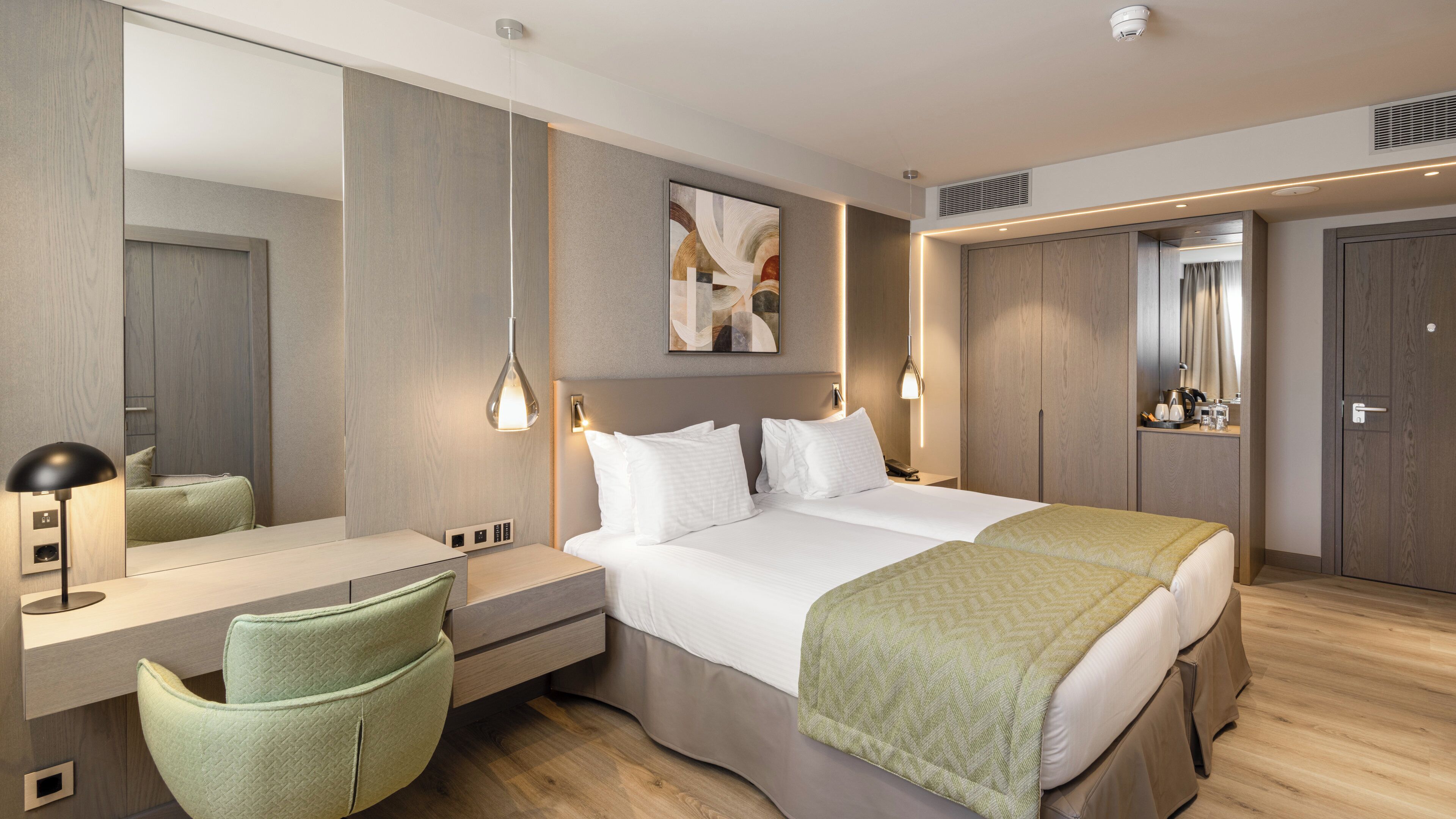 A modern hotel room with a large bed, bedside tables, a desk, a chair, and a large mirror.
