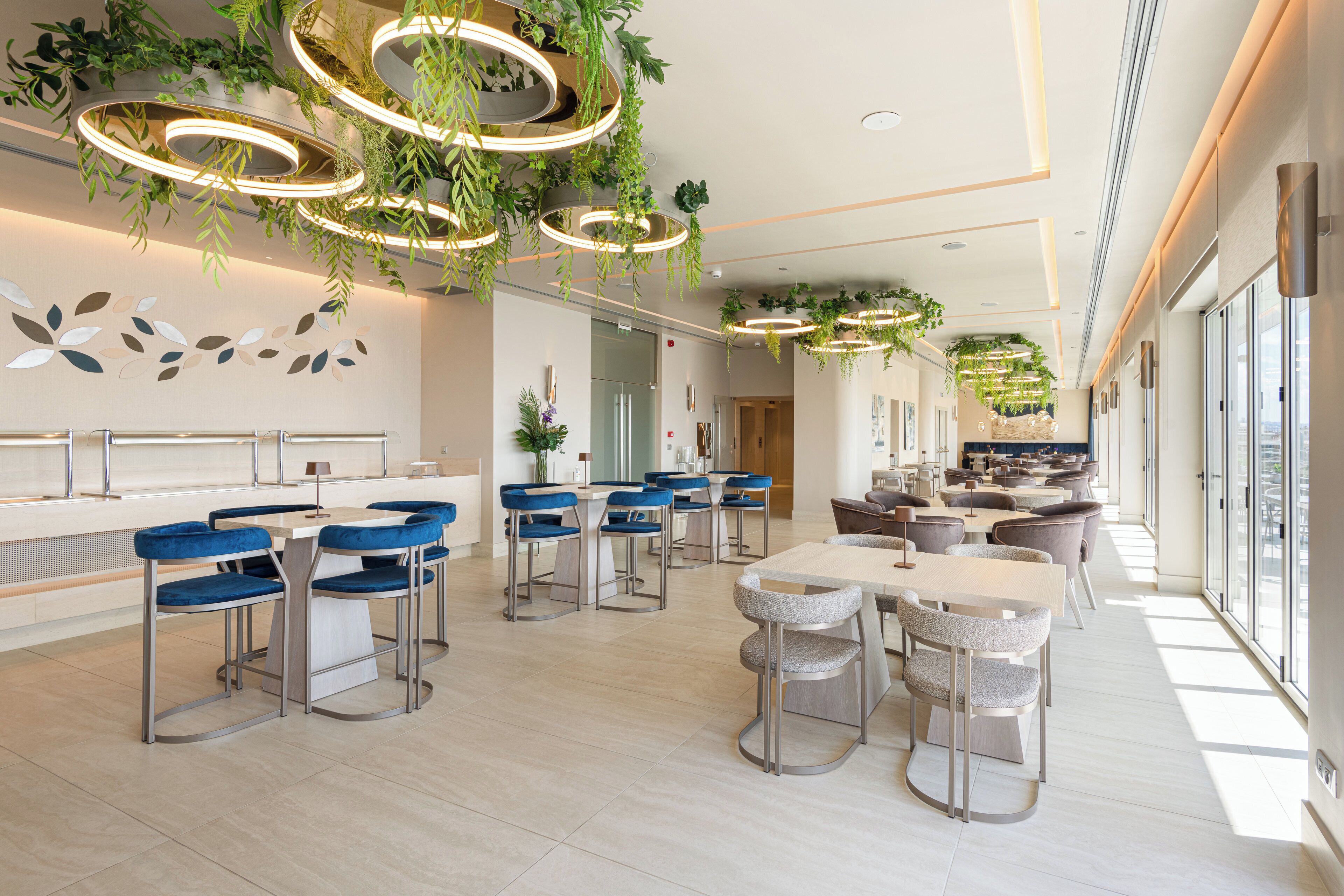 Un restaurante moderno con techos altos, lámparas colgantes circulares y diversas opciones de asientos, incluyendo taburetes de bar y mesas.