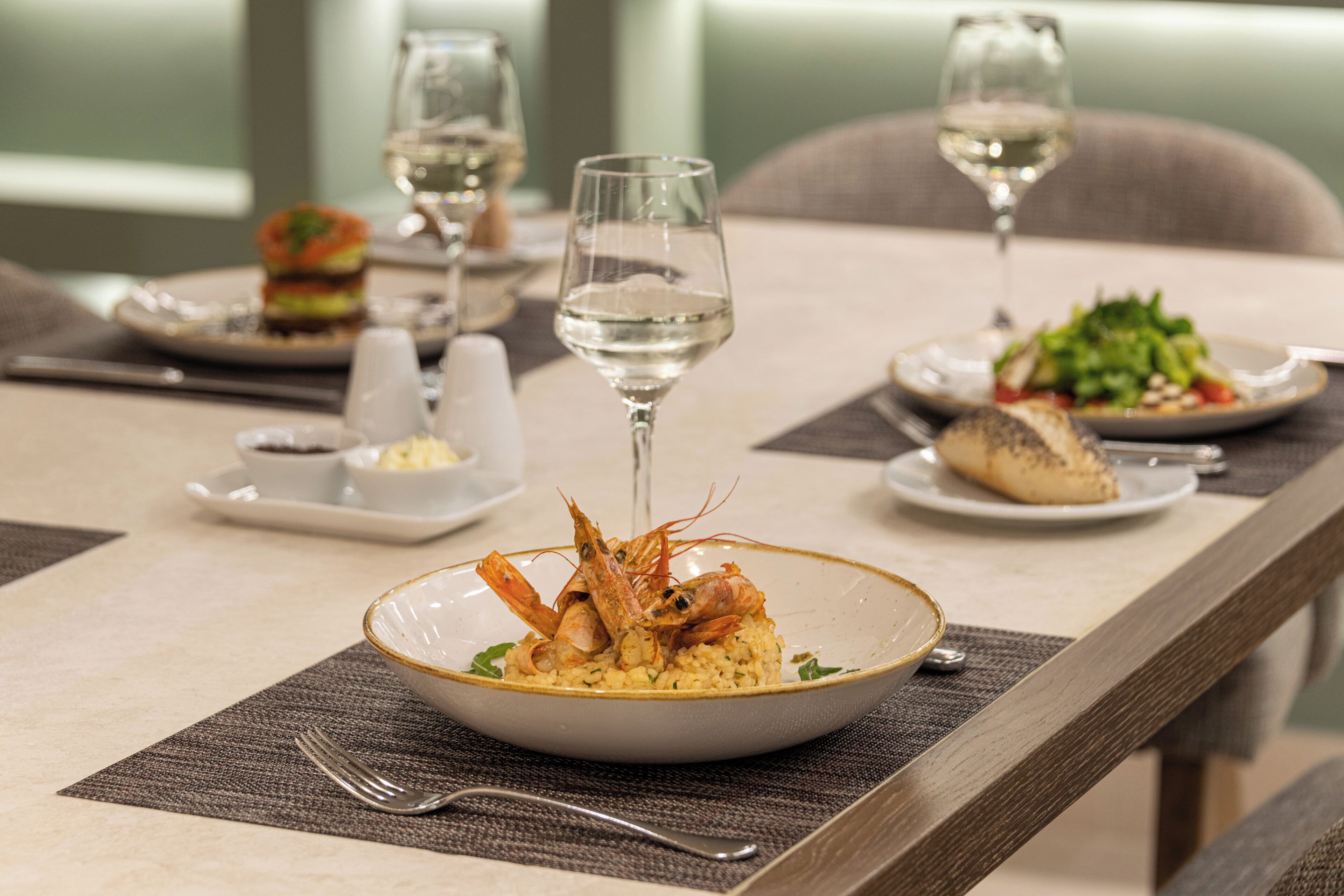 Una mesa con platos de comida, copas de vino y cubiertos.