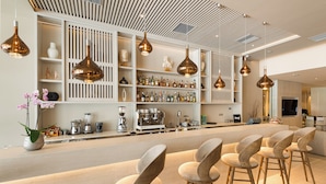 A modern bar area with a long counter, multiple hanging pendant lights, and several bar stools. - Holiday Inn Thessaloniki by IHG (Thessaloniki)
