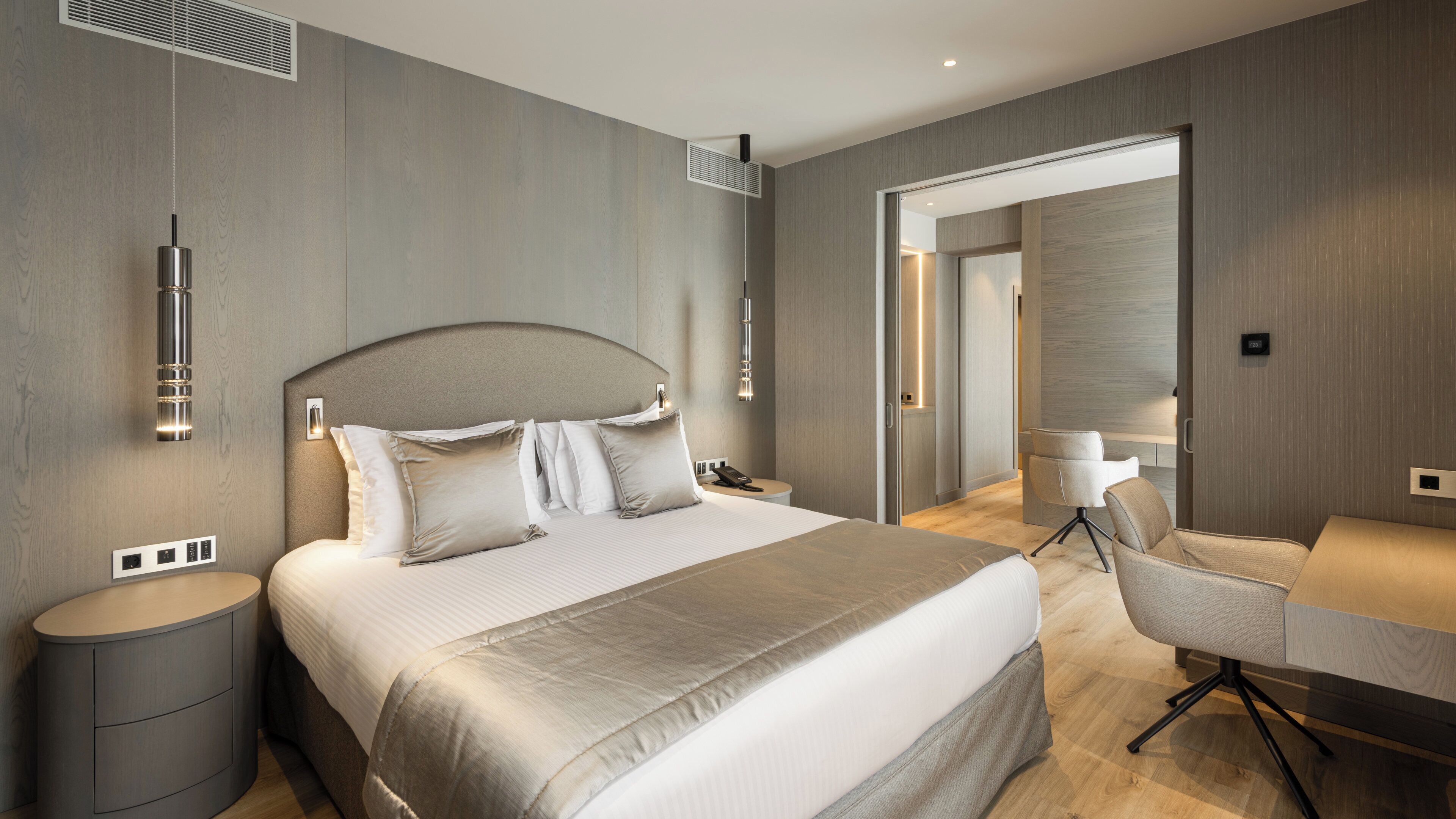 Quarto de hotel moderno com uma cama grande, mesas de cabeceira, uma escrivaninha com cadeira e um closet espaçoso.