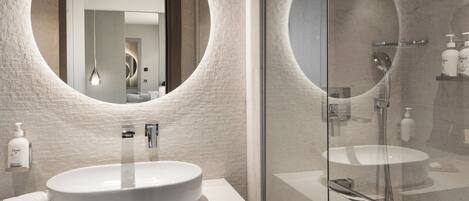 Een moderne badkamer met een grote spiegel in ovaalvorm, een ronde wasbak en een douchecabine met glazen wanden.
