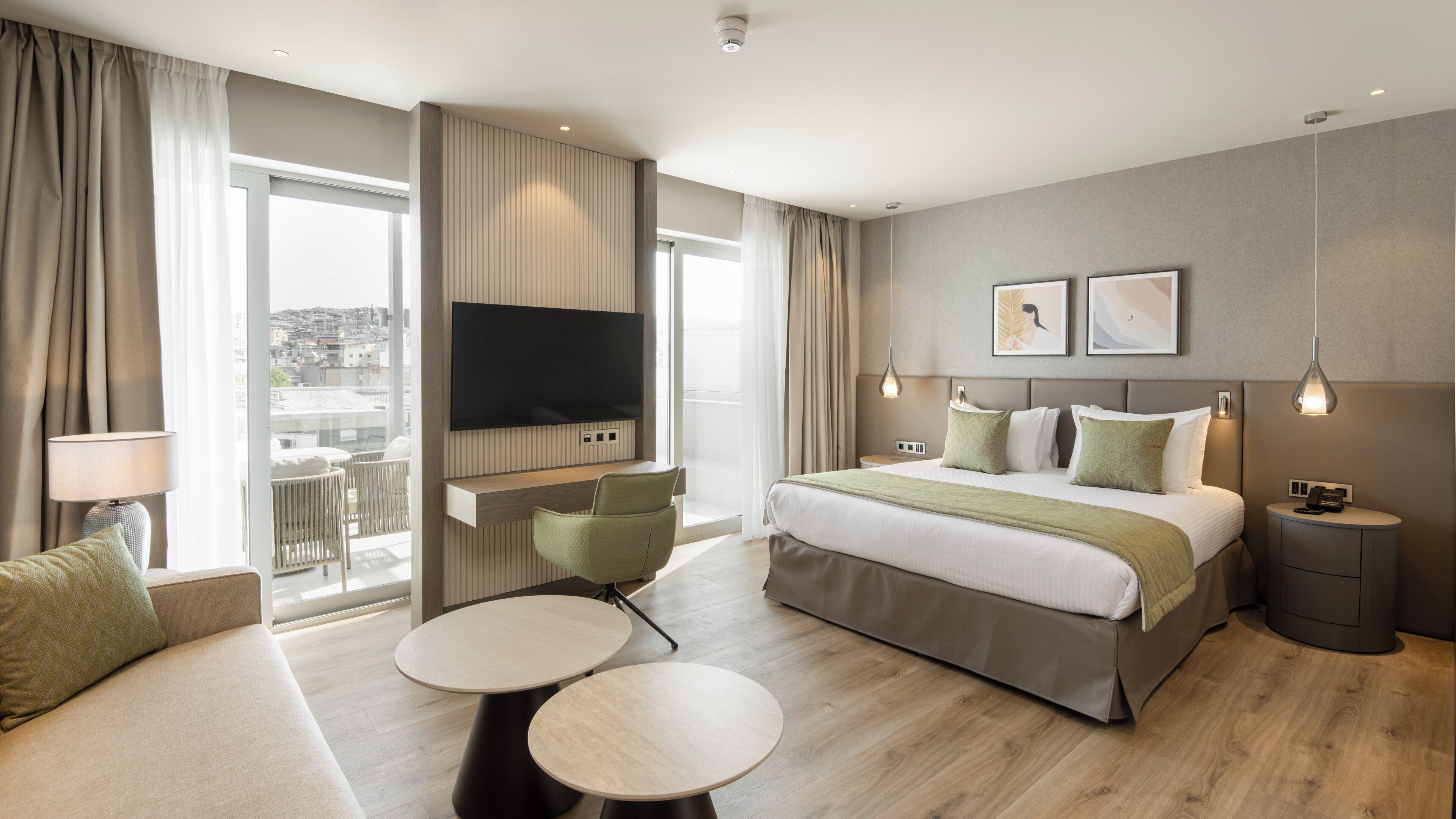 Una habitación de hotel moderna con una cama grande, un televisor de pantalla plana, un balcón con vistas y un pequeño comedor.