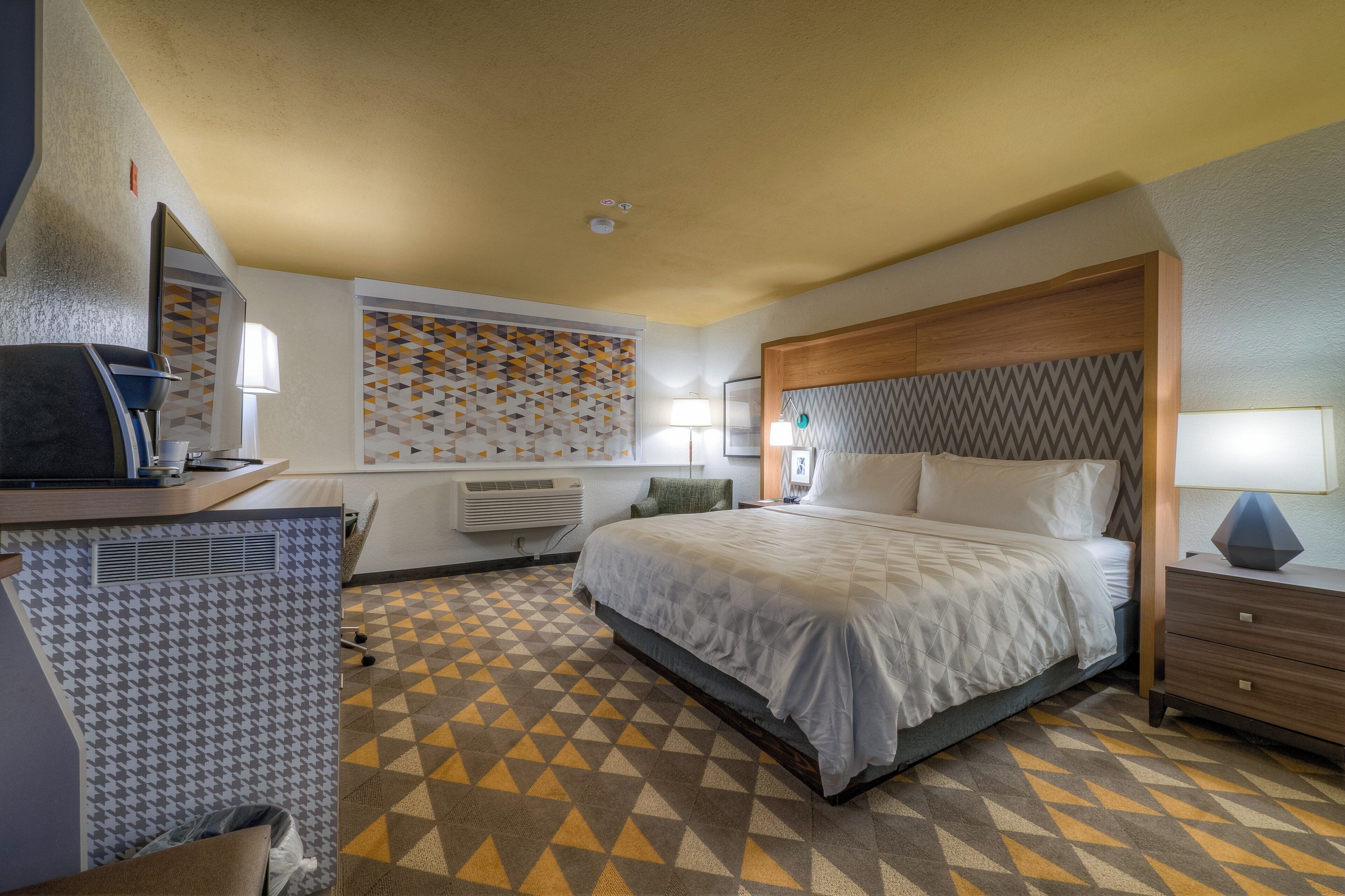 Hotellihuone, jossa on sänky, työpöytä, tuoli ja kuviollinen lattia.