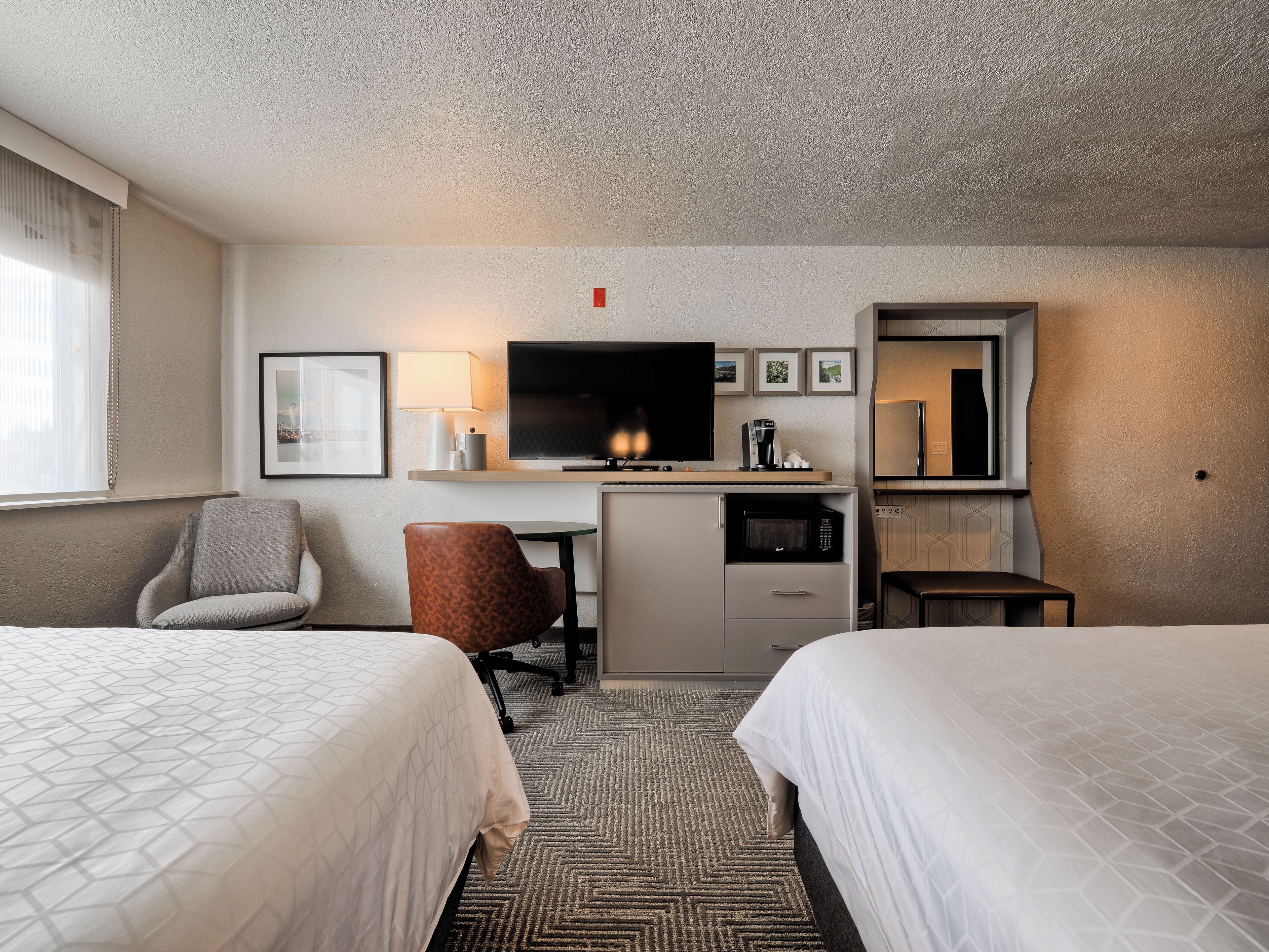 Quarto de hotel com duas camas, uma escrivaninha com televisão, micro-ondas e máquina de café.