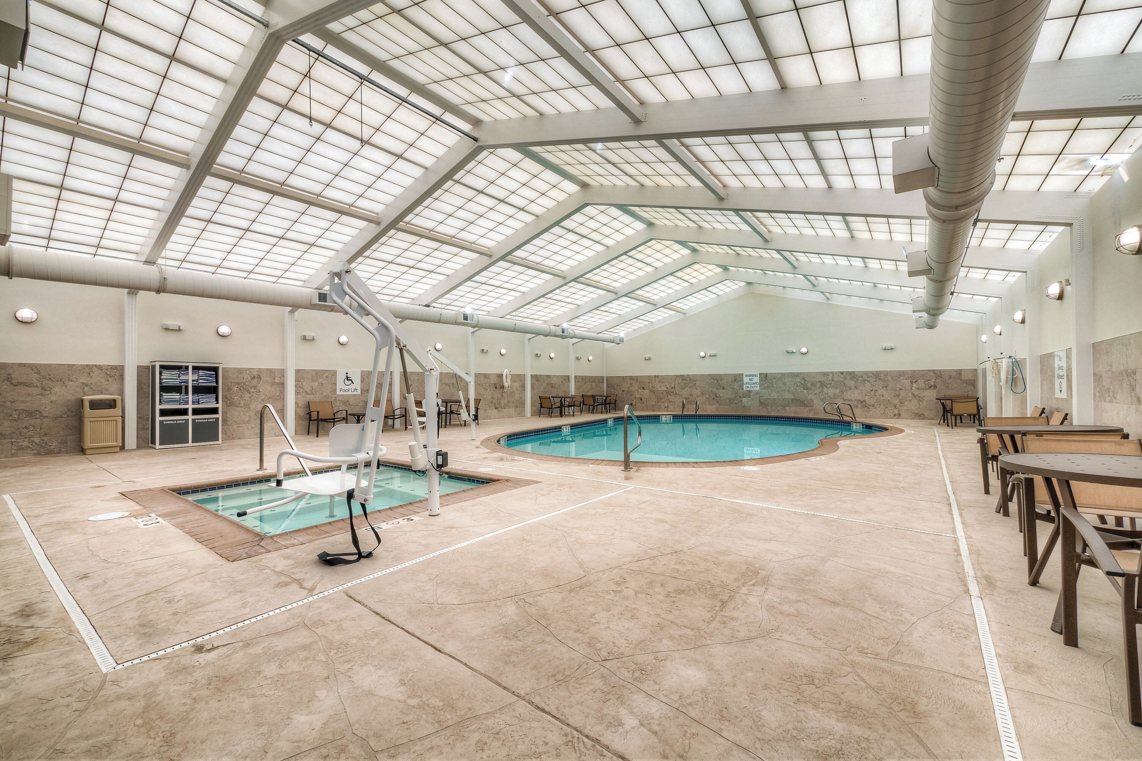 Una piscina interior con techos altos y tragaluces, rodeada de asientos y una estación de salvavidas.