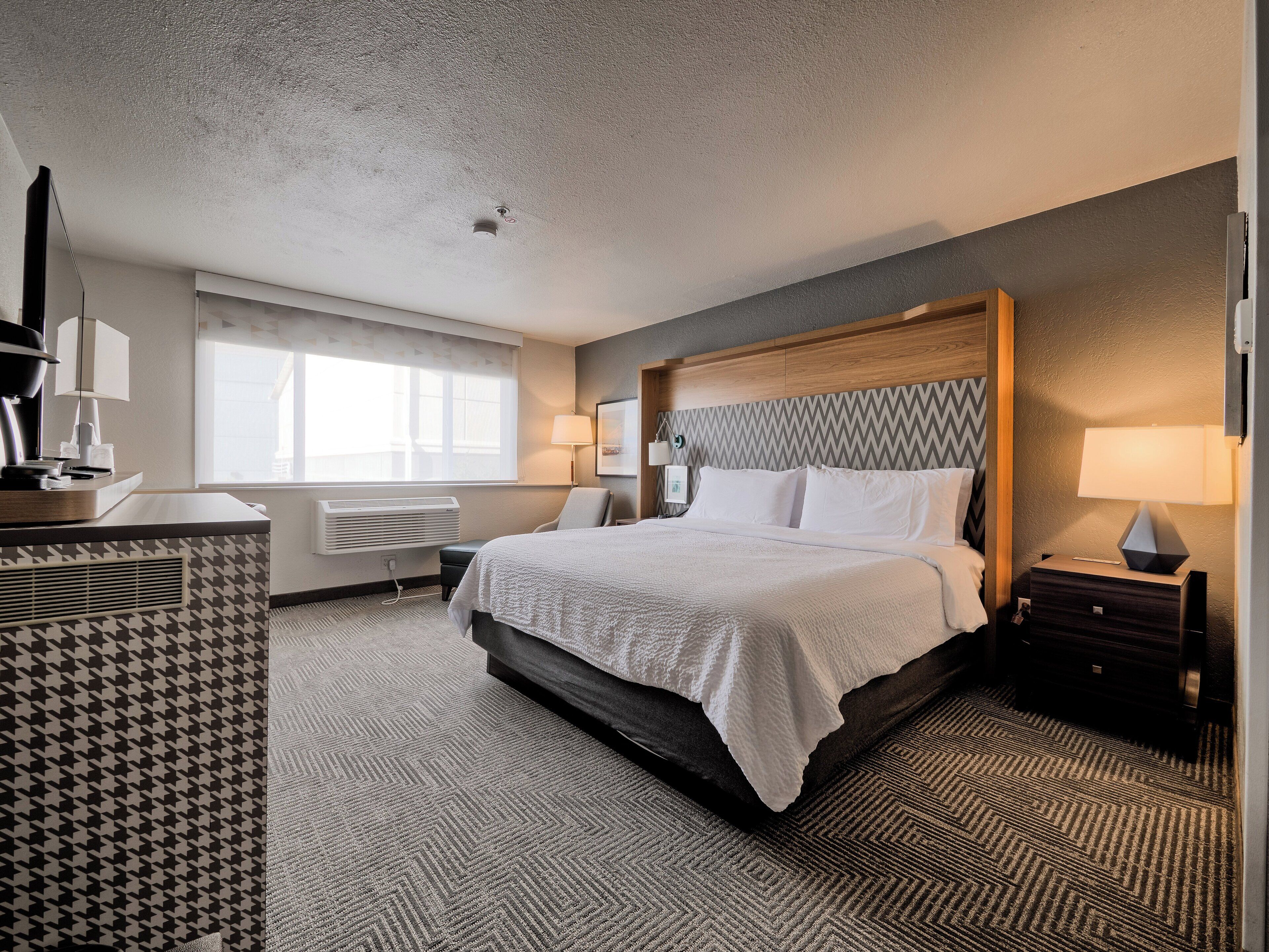 Une chambre d’hôtel avec un lit, des tables de chevet, un bureau et une fenêtre.