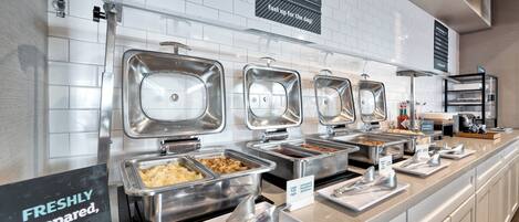 Montaje de bufé con diversas estaciones de comida, incluyendo un cartel que dice "PREPARADO AL MOMENTO, solo para ti".
