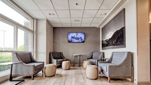 A modern waiting area with comfortable seating, a flat-screen TV, and a large window offering a view of the outdoors. - Holiday Inn Tacoma Mall by IHG (Tacoma)