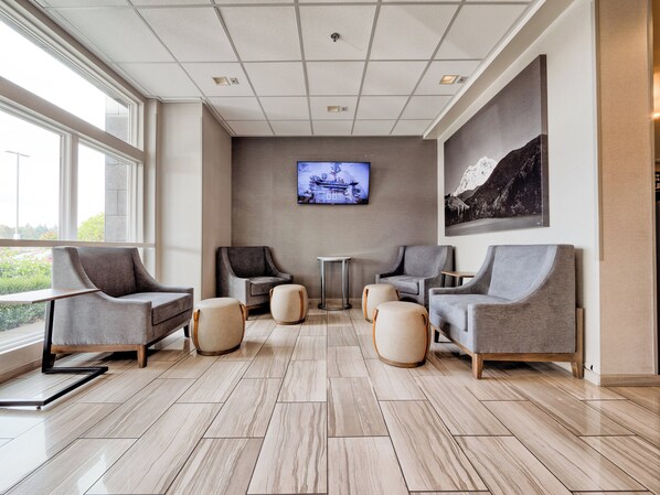 A modern waiting area with comfortable seating, a flat-screen TV, and a large window offering a view of the outdoors.