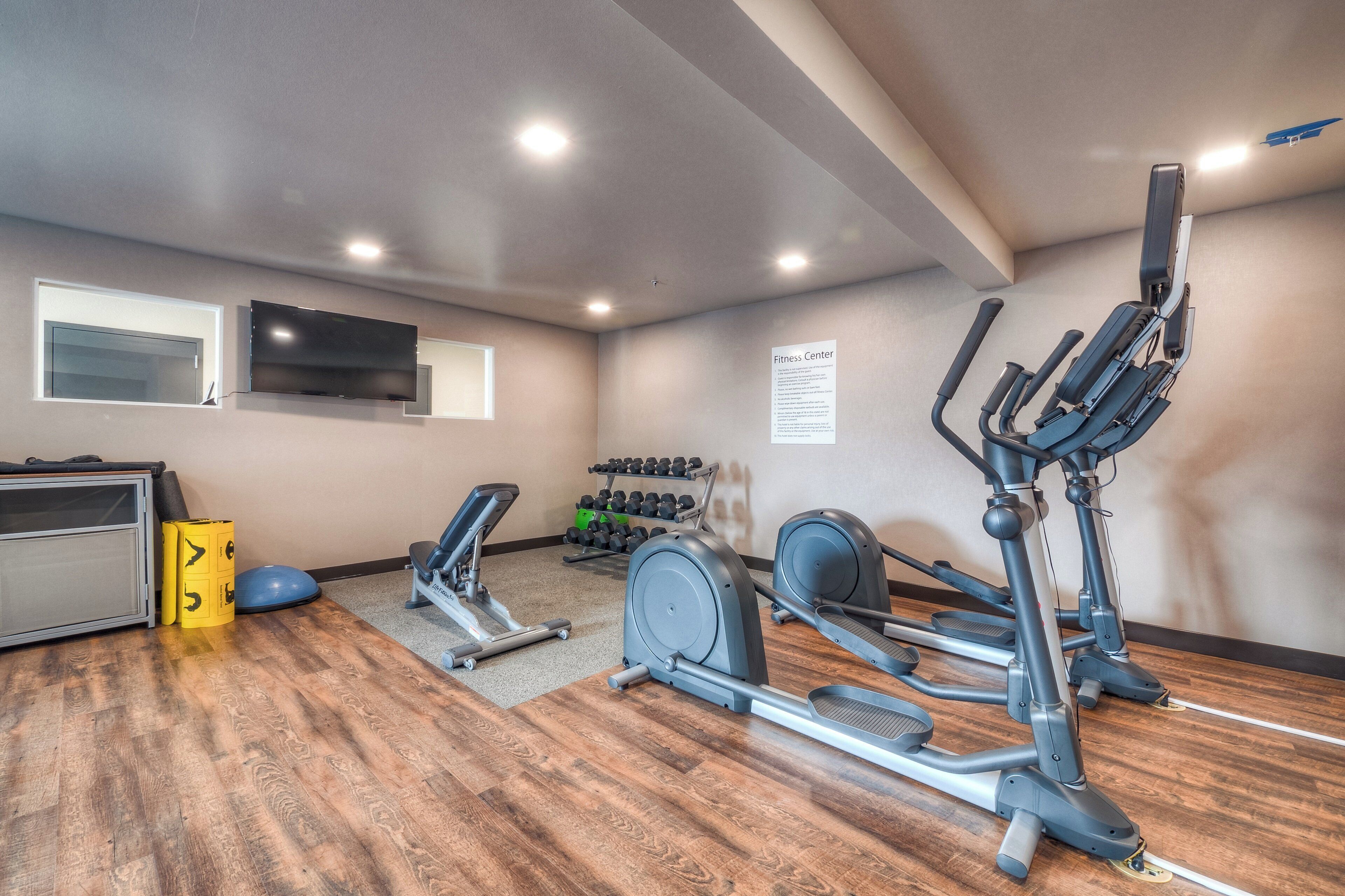 A fitness center with exercise equipment, a television, and a sign detailing the center's rules.