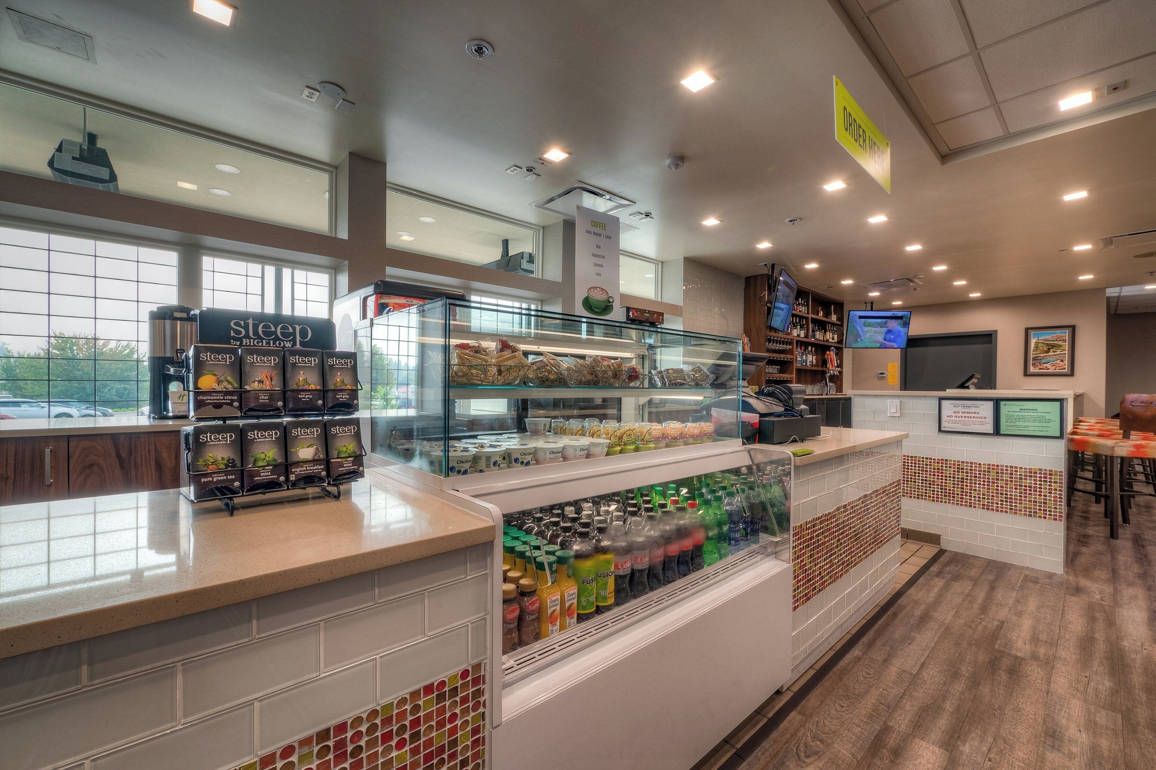 A coffee shop interior with a display of 'steep' tea boxes, a coffee station, and a beverage refrigerator.