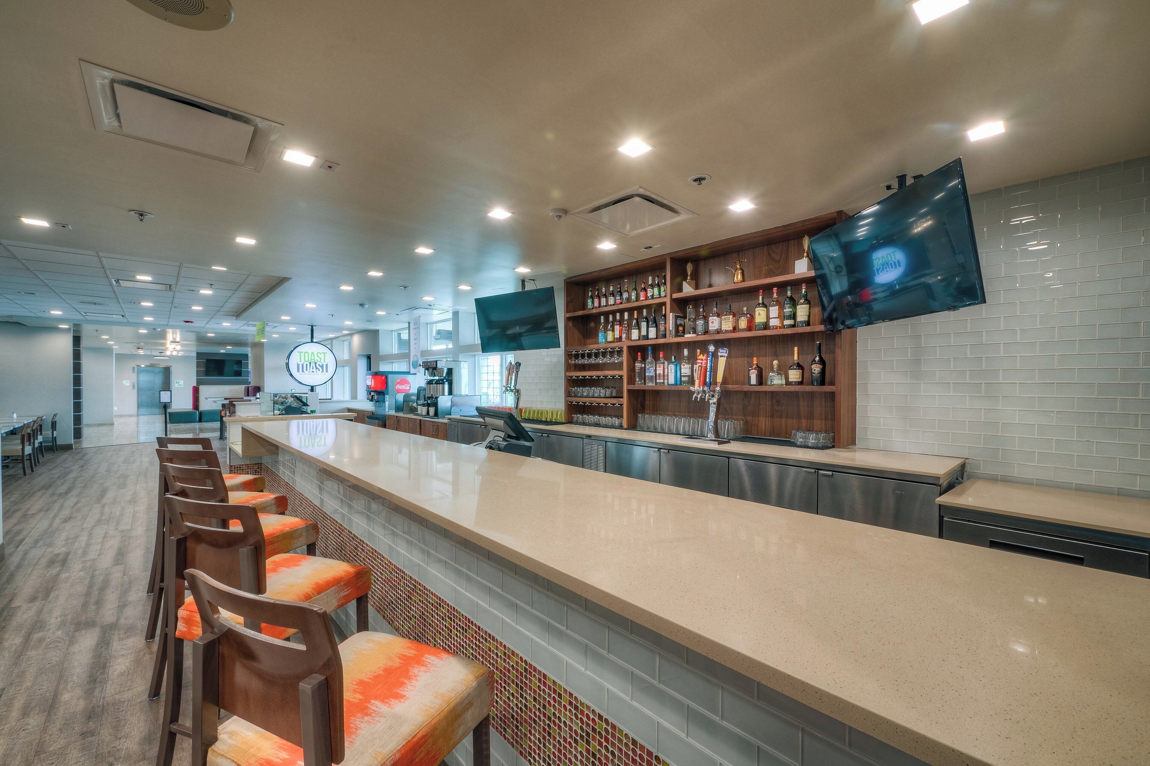 Un espace bar avec un long comptoir, des tabourets de bar et un téléviseur fixé au mur.