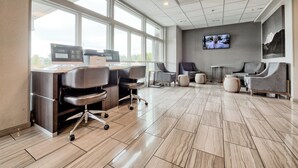 A modern office space with a large desk, multiple chairs, a television, and a view through large windows. - Holiday Inn Tacoma Mall by IHG (Tacoma)