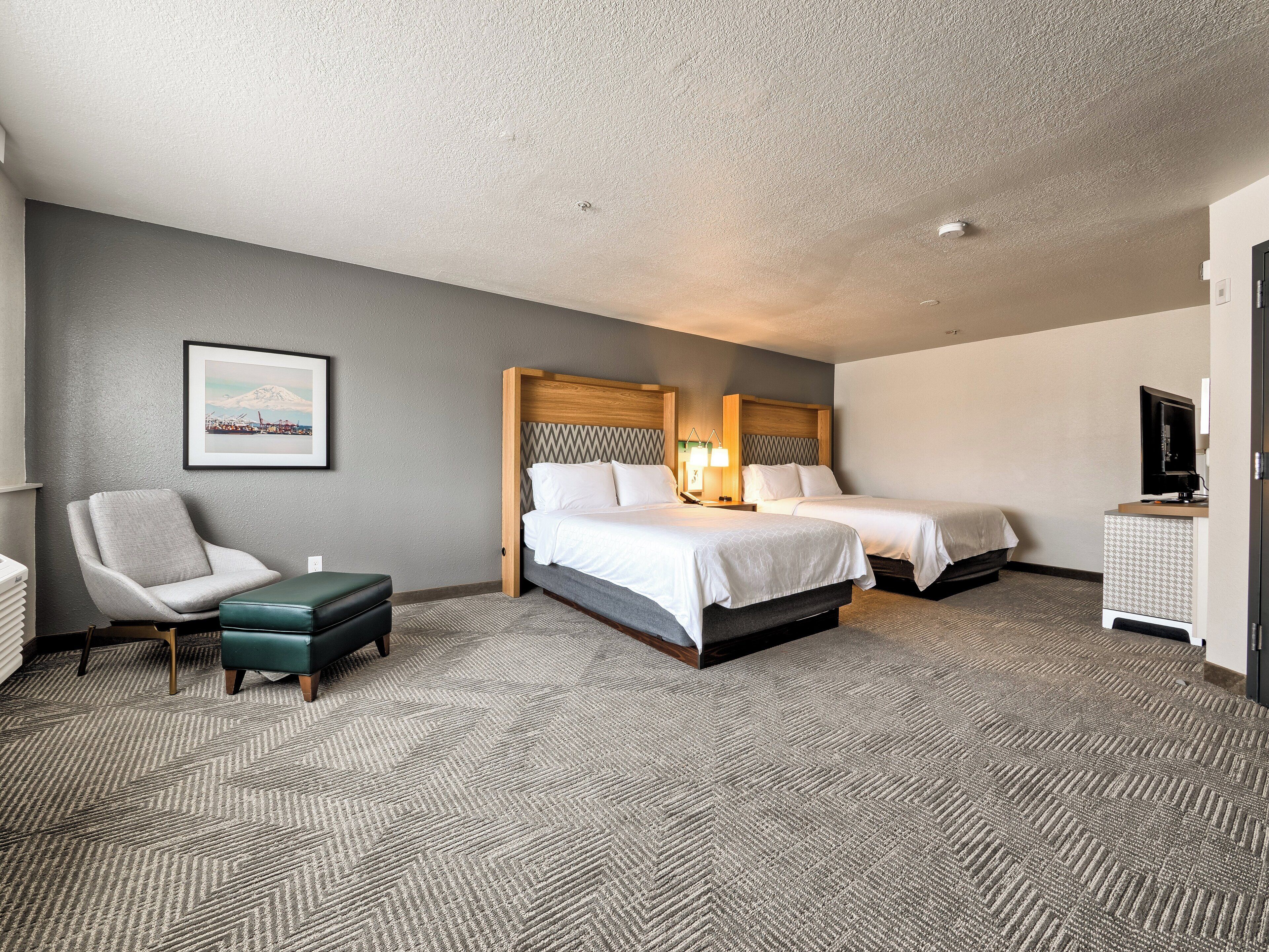 A hotel room with two beds, a chair, a desk, and a television.