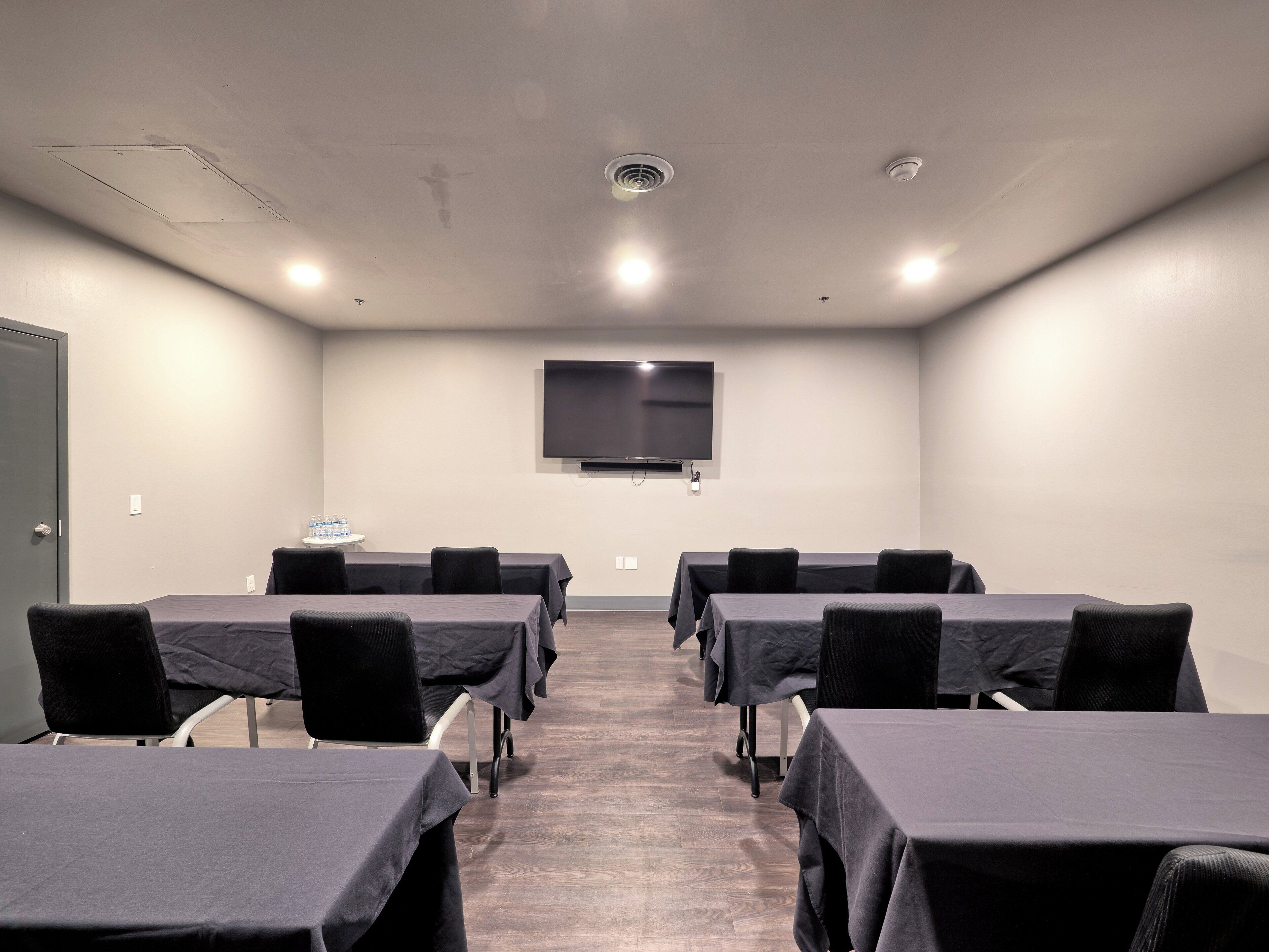 Una sala de conferències amb taules, cadires, un televisor de pantalla plana i una porta.