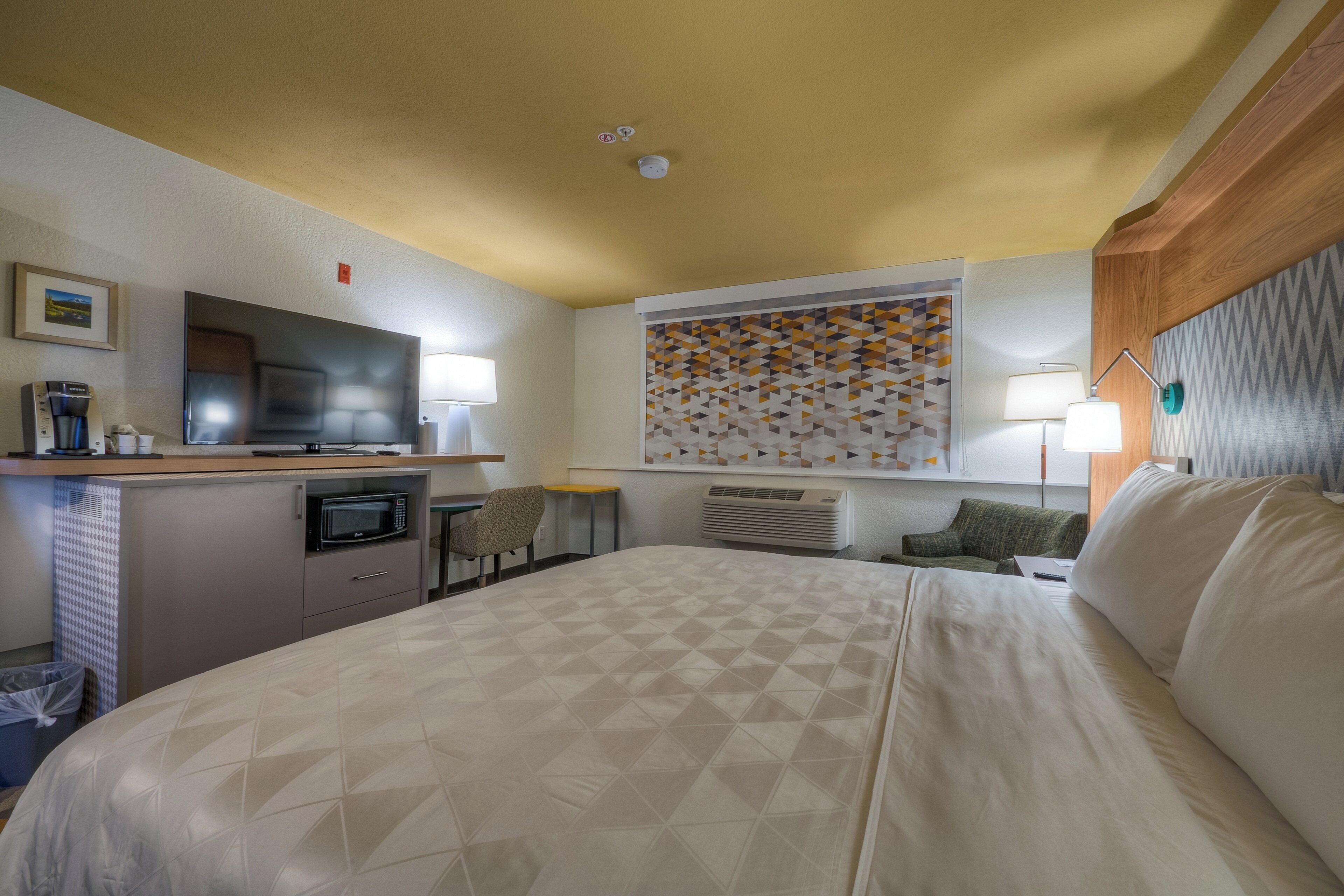 A hotel room with a bed, a television, a coffee machine, a microwave, a desk, and a chair.