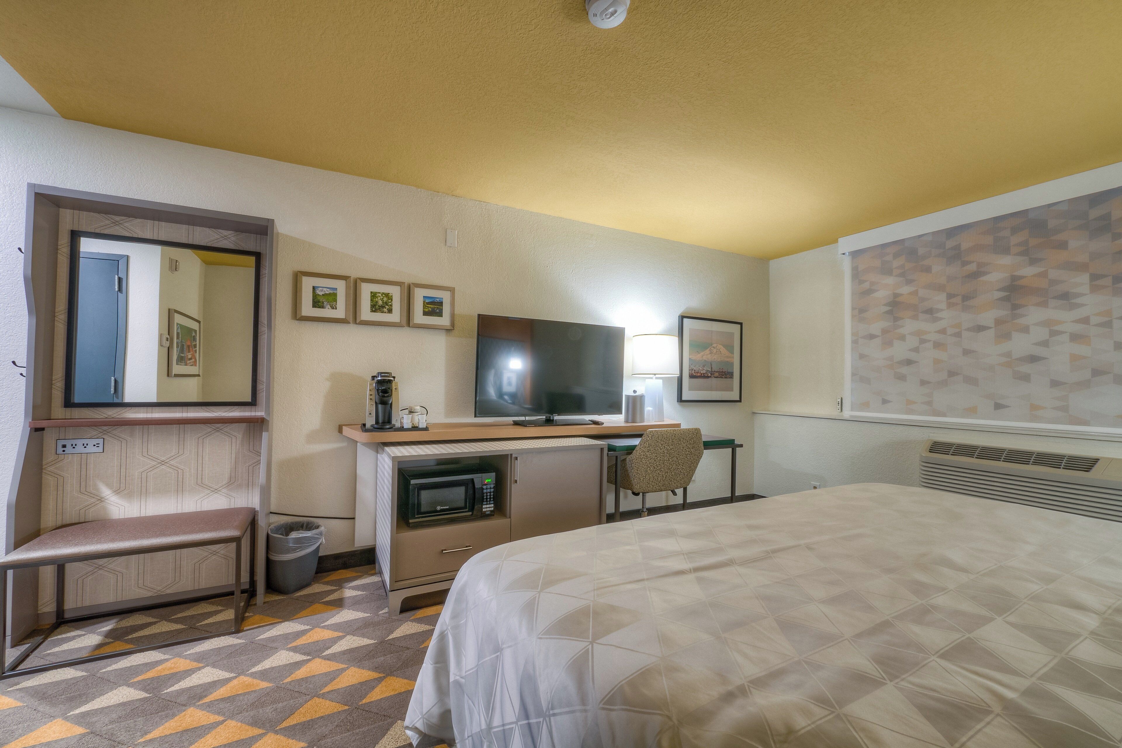 A hotel room with a bed, desk, chair, television, and a mirror.