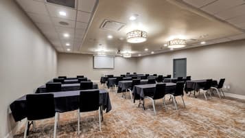 A conference room with rows of tables and chairs, a projector screen, and a patterned carpet.