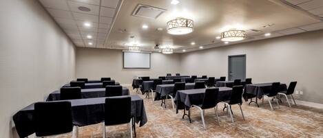 A conference room with rows of tables and chairs, a projector screen, and a patterned carpet.
