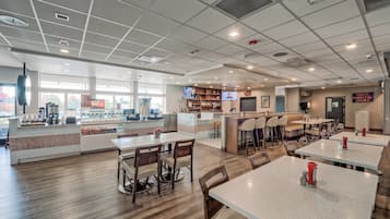 Una cafetería espaciosa con varias zonas de estar, una barra de café y una pantalla de televisión.