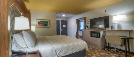 A hotel room with a bed, desk, chair, TV, and a microwave.