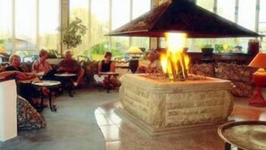A lobby with a central stone fireplace, seating areas, and large windows. - Lycus River Thermal Hotel (Denizli)