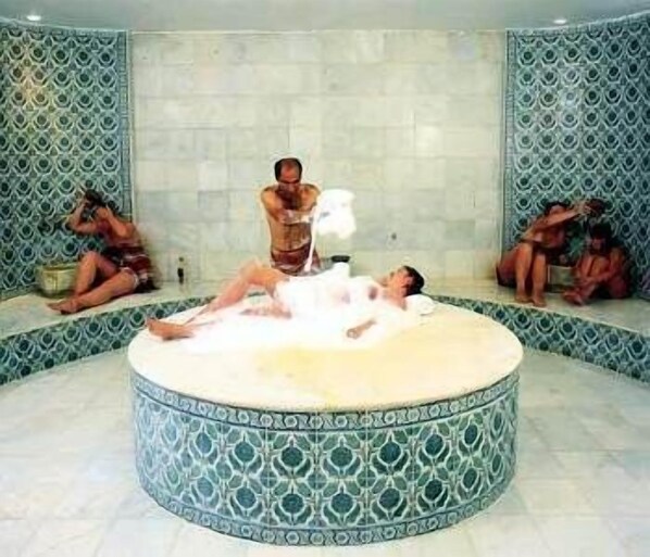 En rund jacuzzi med en person stående og en anden liggende, omgivet af mønstrede vægge.