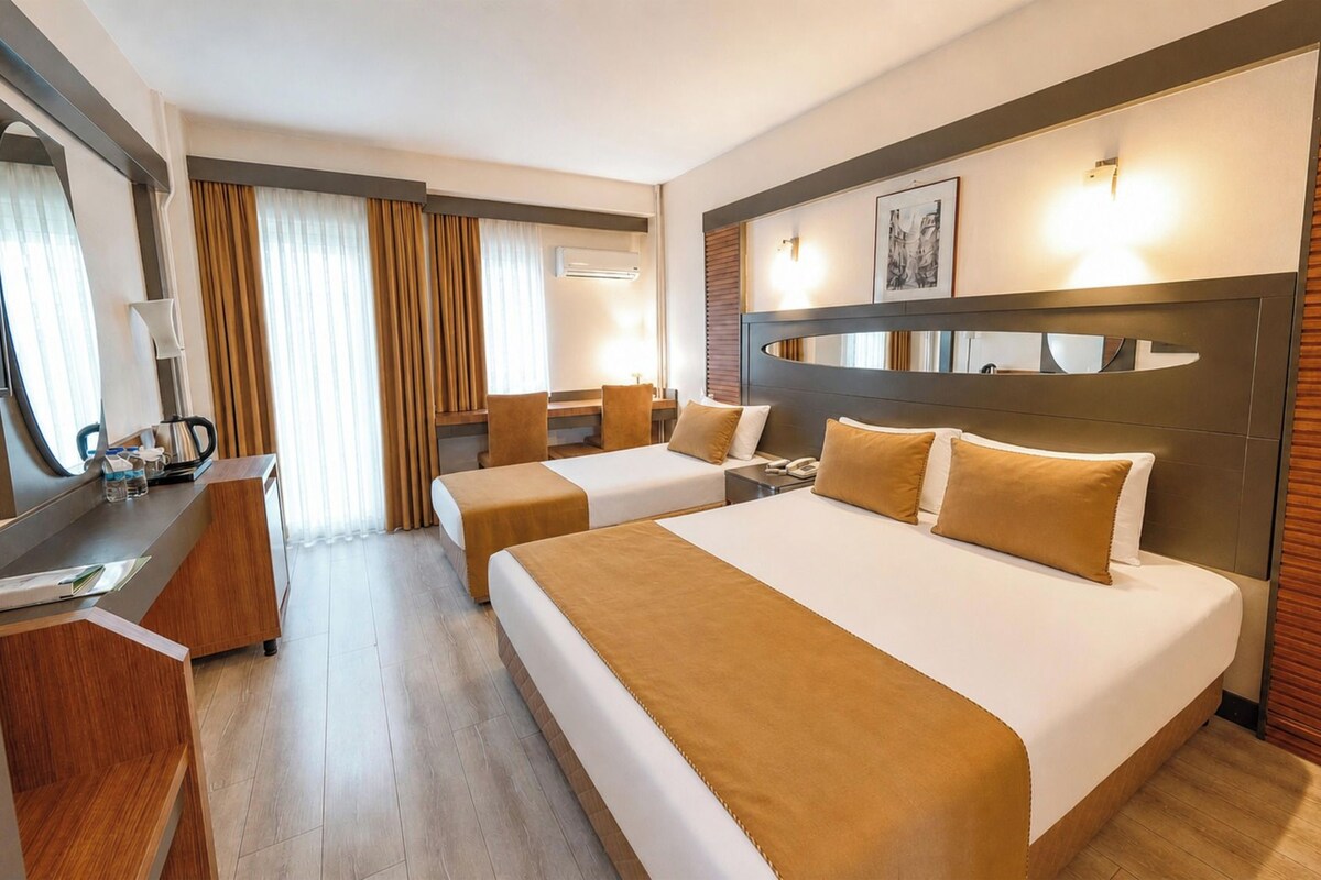 A hotel room with two beds, a desk, a chair, a mirror, and a window with curtains.