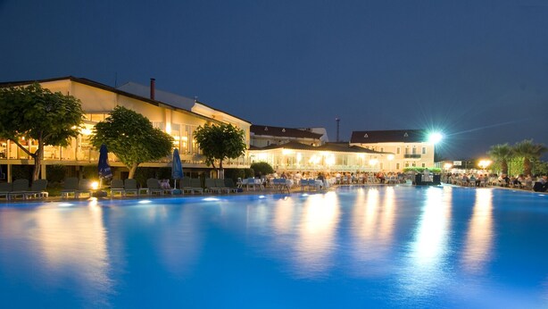 A nighttime view of a swimming pool area with lounge chairs and tables, surrounded by buildings with warm lighting. - Lycus River Thermal Hotel (Denizli)