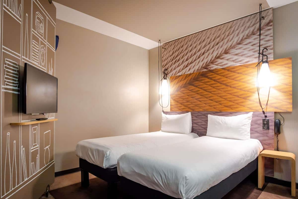 Een hotelkamer met een bed, een televisie, een muur met een geometrisch patroon en een hanglamp.