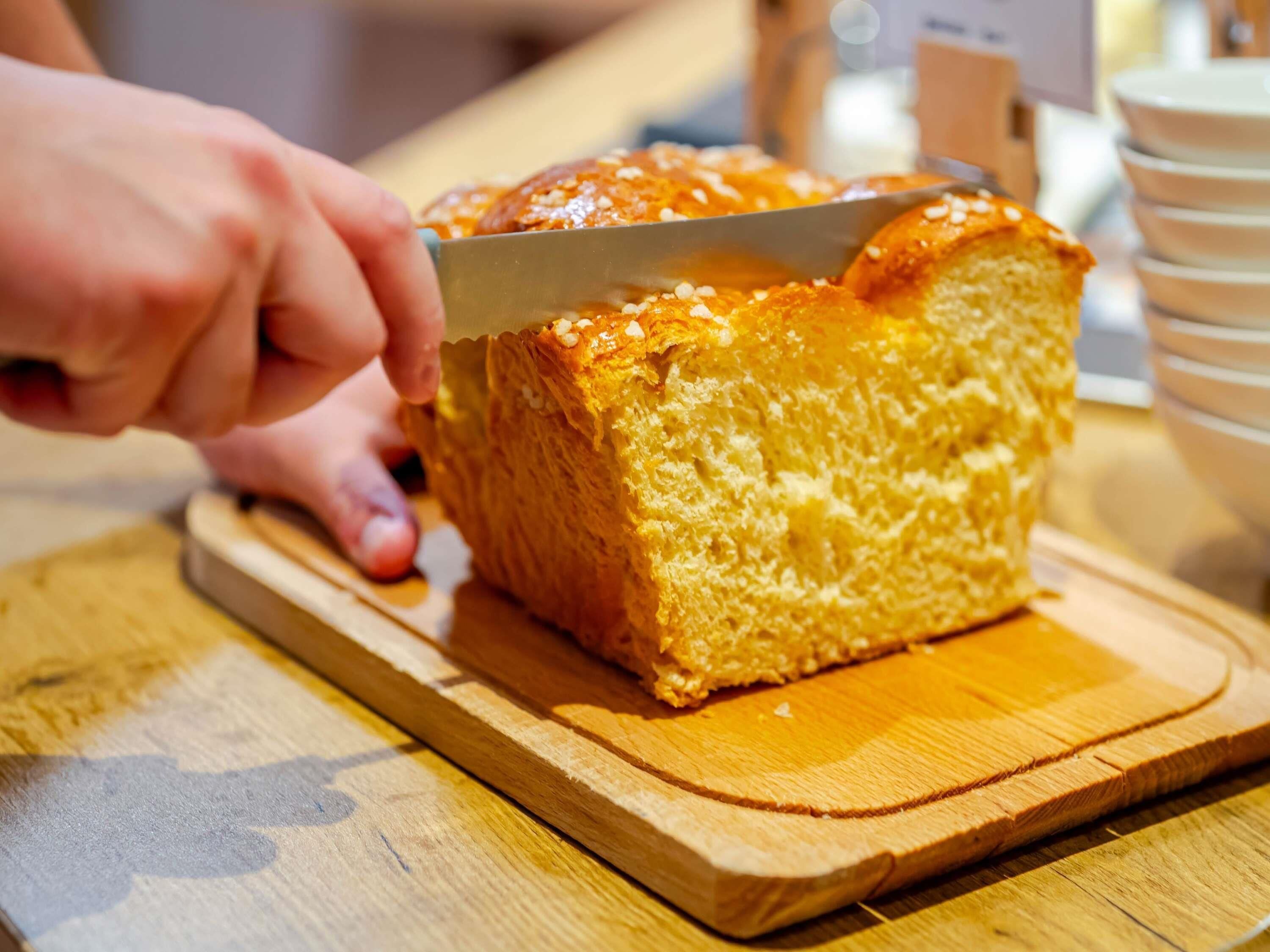 A loaf of bread being sliced on a wooden cutting board.