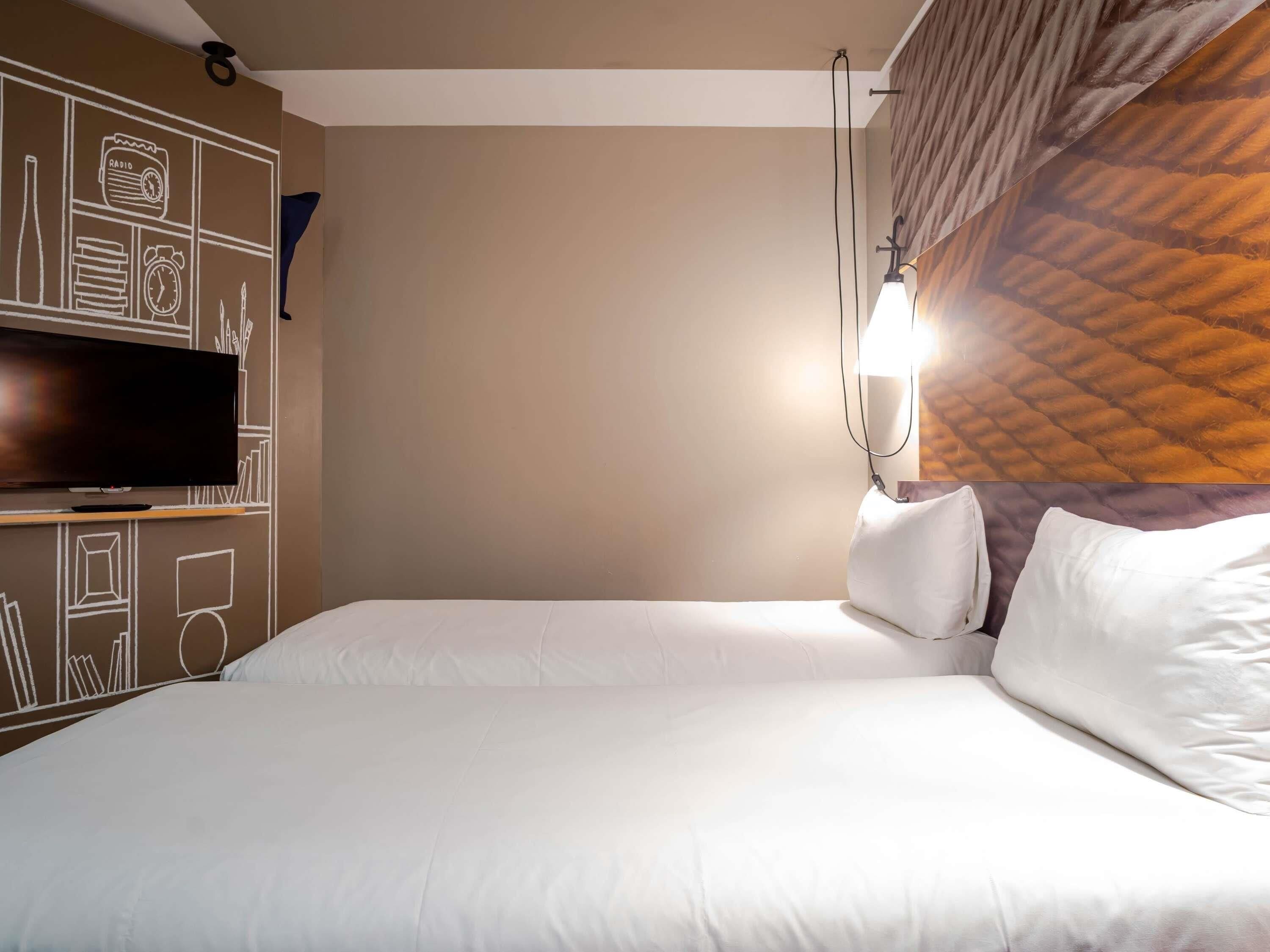 Ein Hotelzimmer mit Bett, Fernseher auf einem Schrank und Wand mit geometrischem Muster.