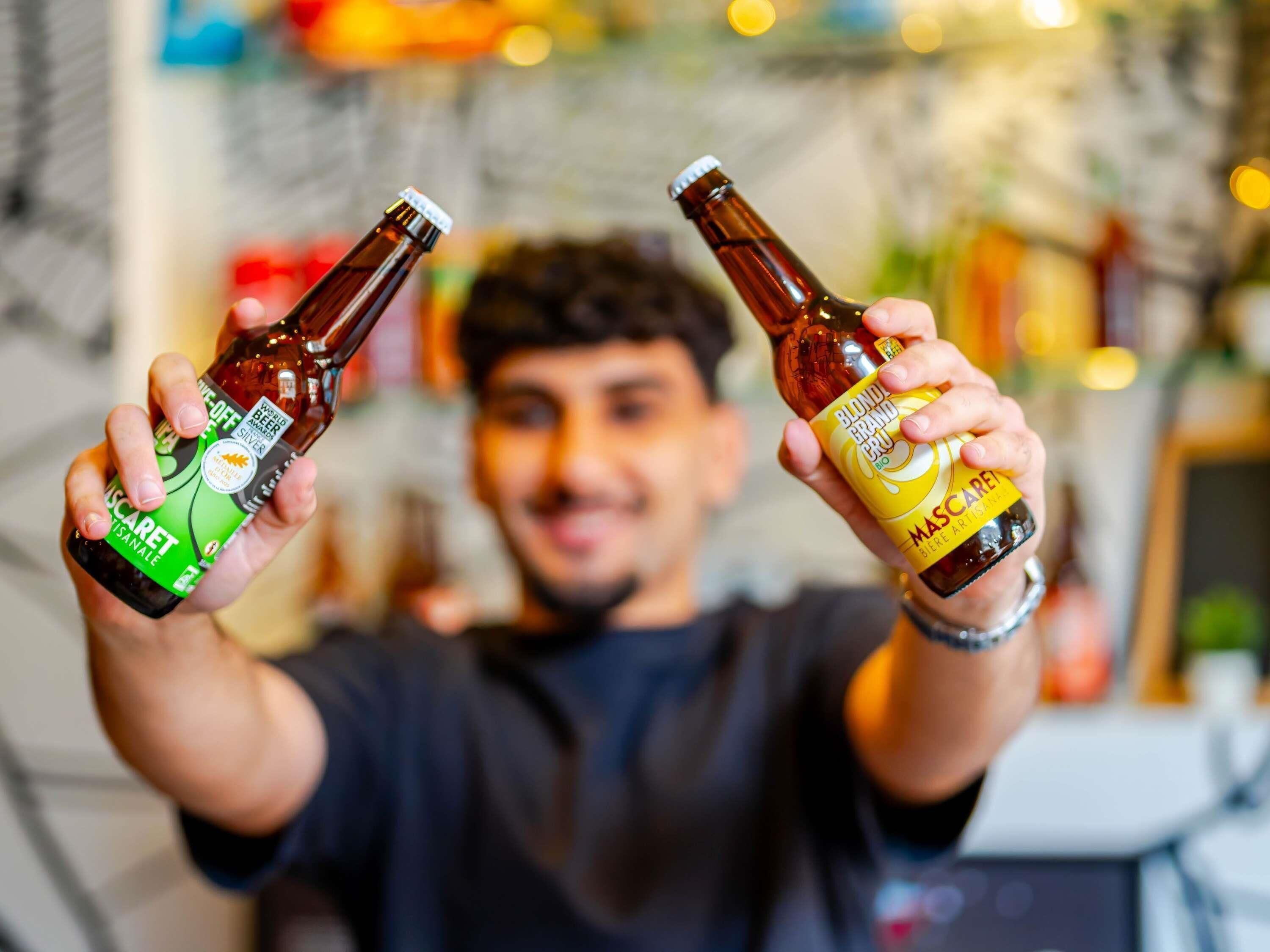 A person holding two bottles of beer, one labeled 'Blondie Grand Bru' and the other 'Scare Tansale.'